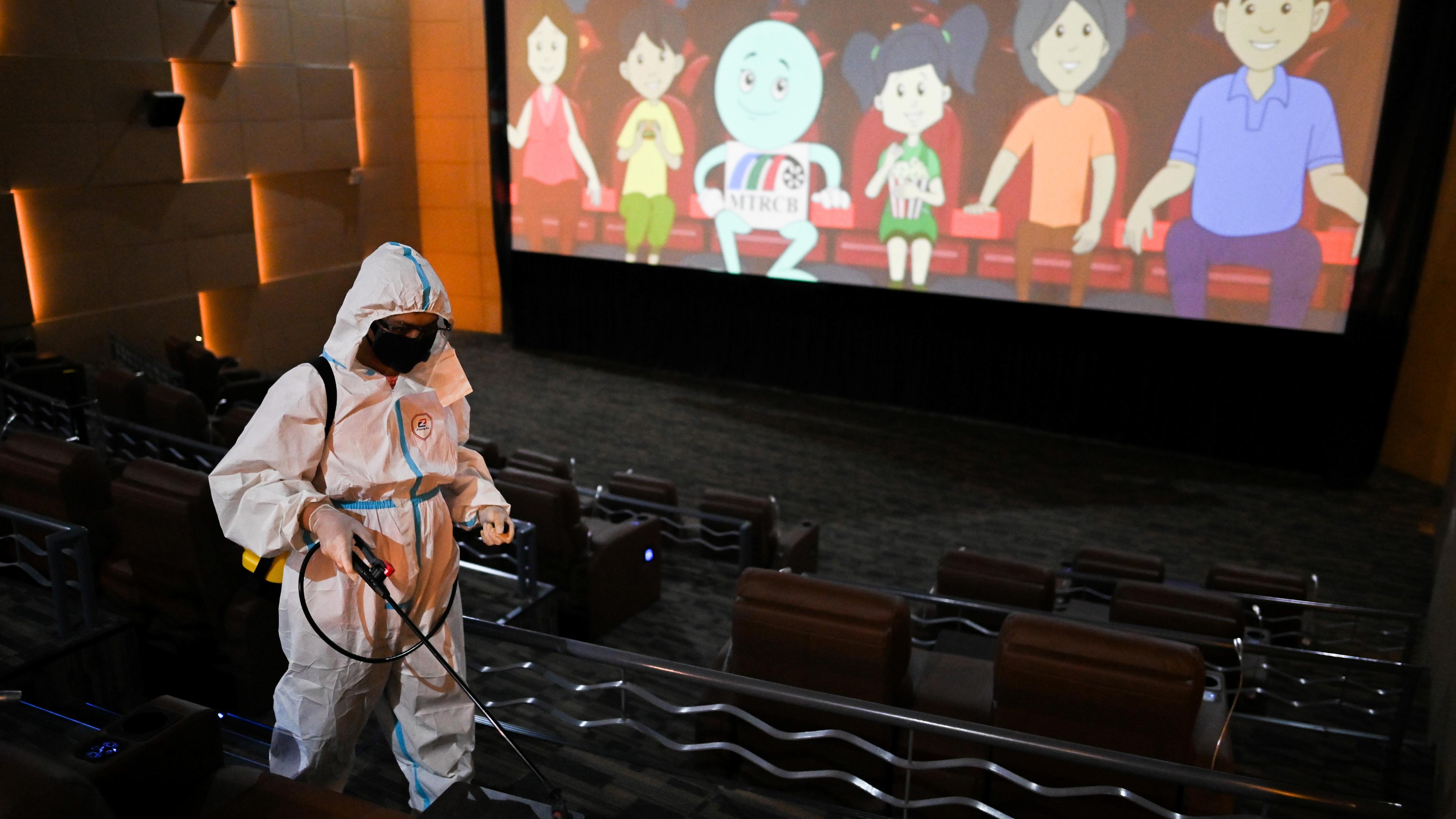 Photo of a person in protective gear disinfecting an empty cinema with an animated film playing on the screen.