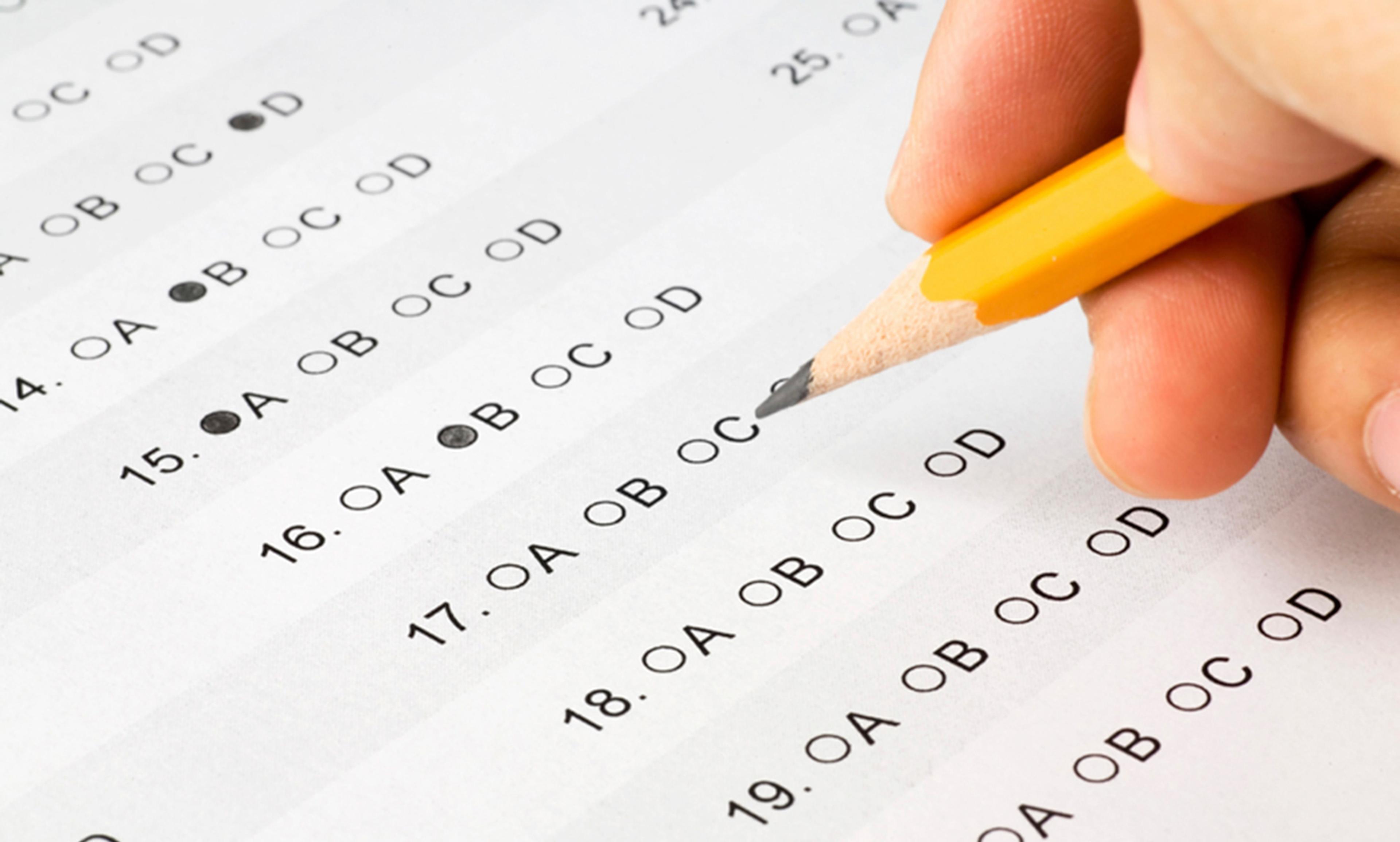 A multiple-choice test with a pencil marking option C. The hand holds a yellow pencil above an answer sheet.
