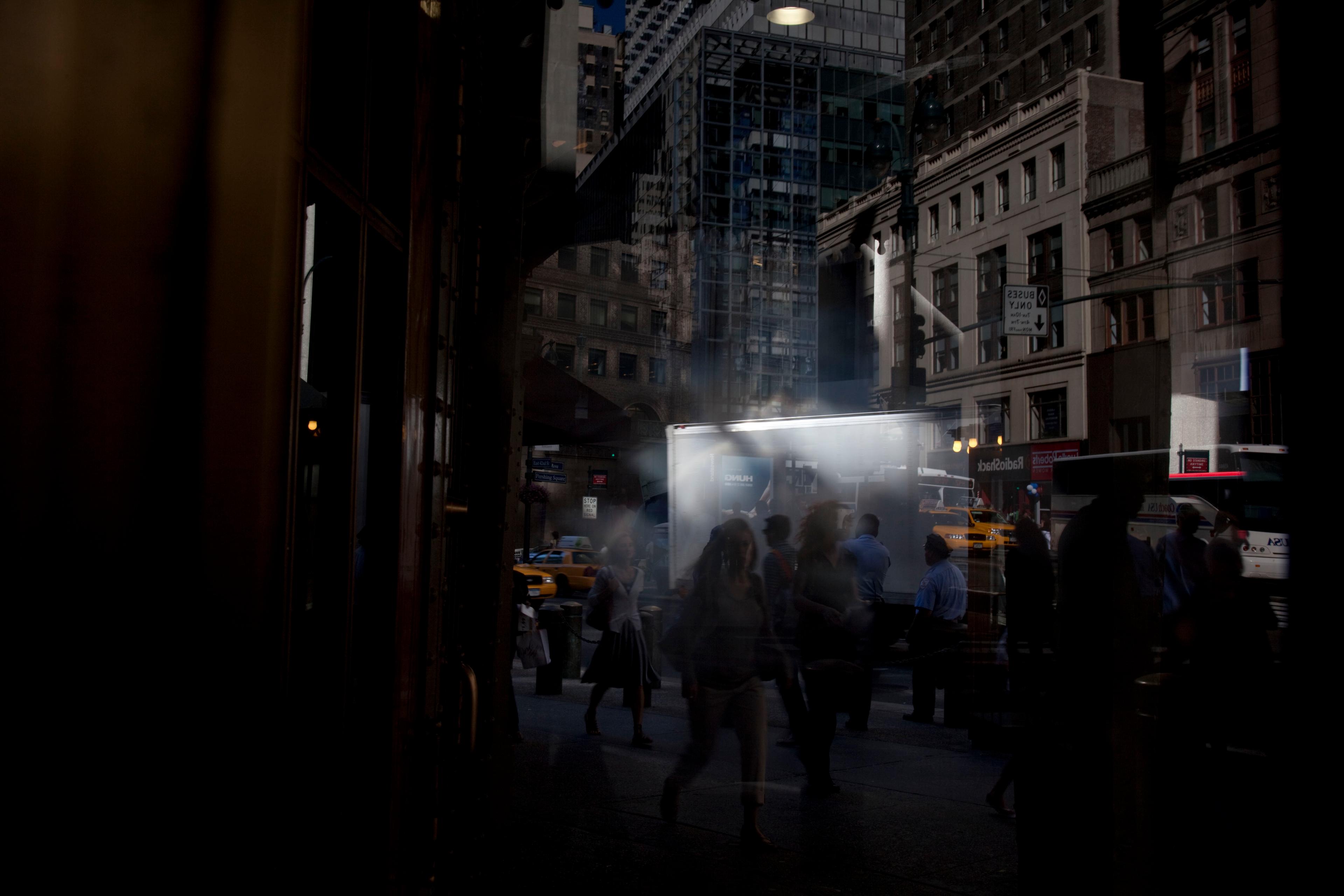 Photo of a busy city street with blurred pedestrians and taxis at dusk, reflected in a glass window.