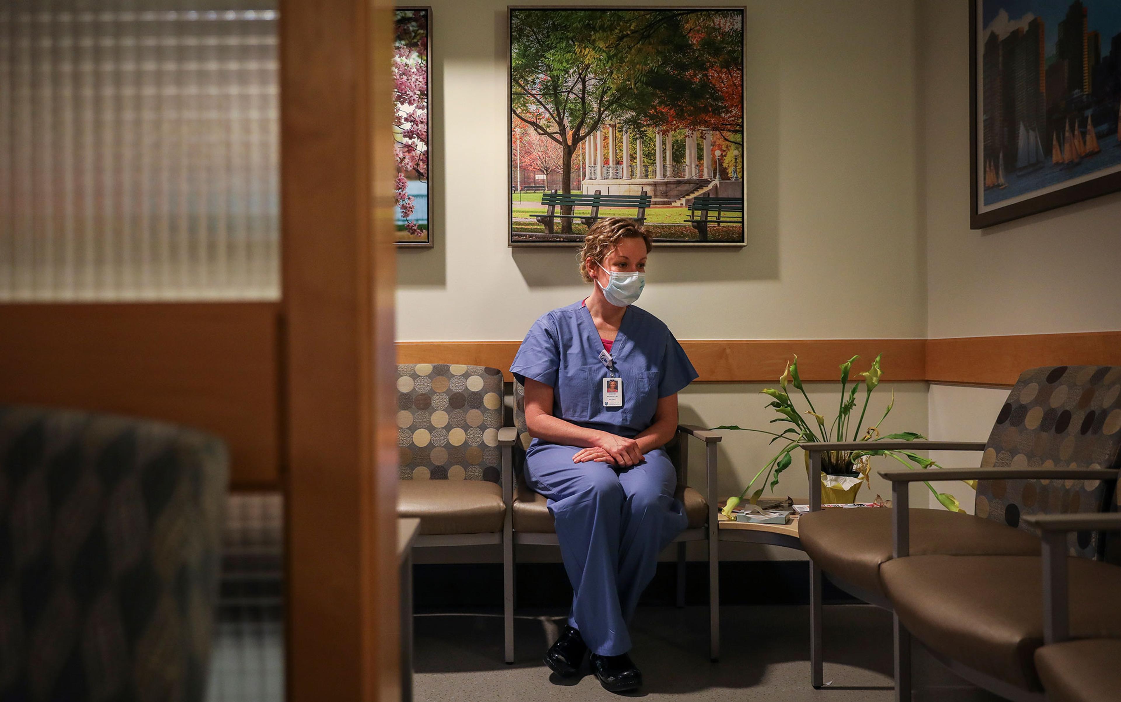 A masked nurse in scrubs sitting in a hospital waiting area.