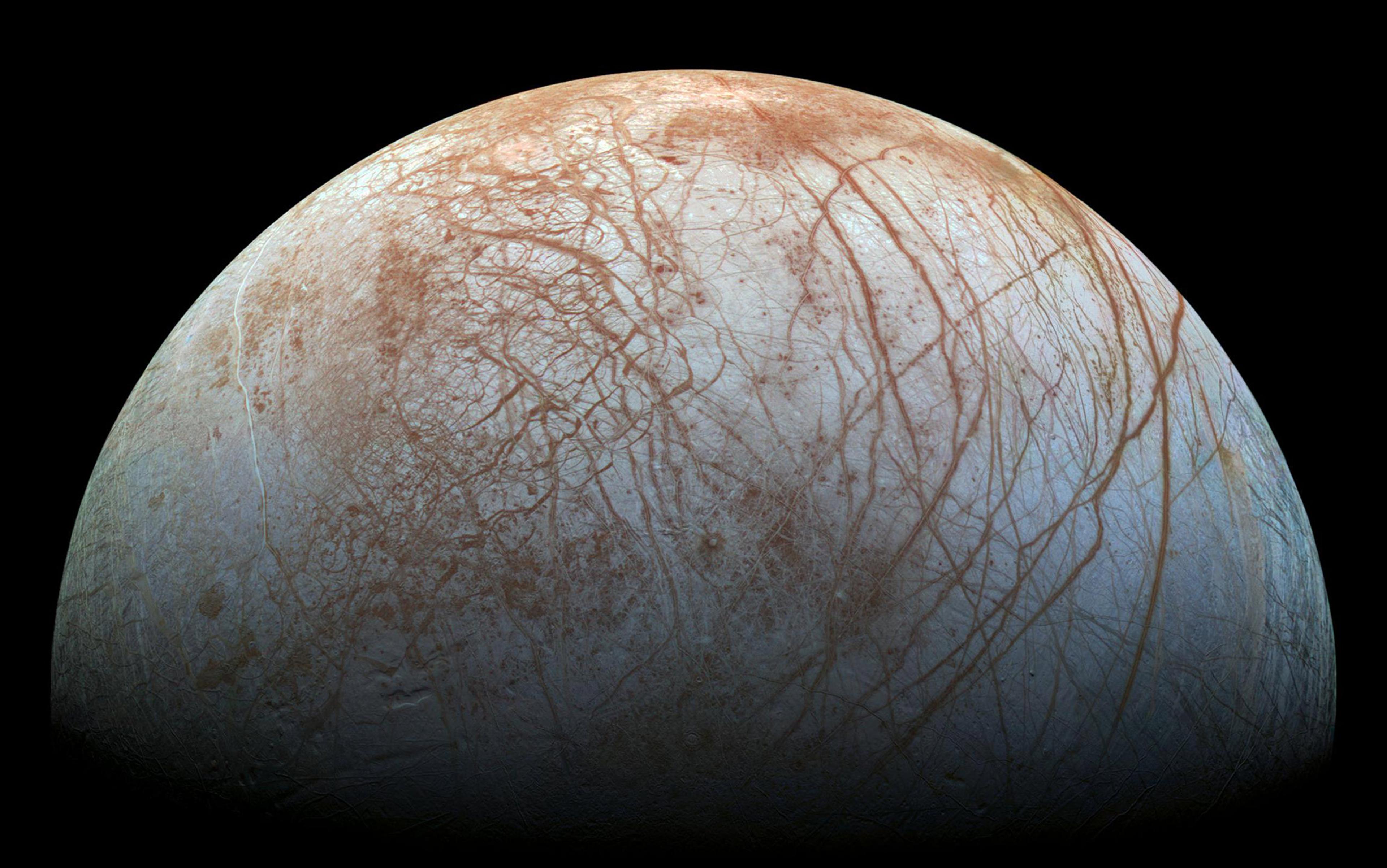 Photo of Jupiter’s moon Europa with a surface covered in reddish-brown lines and patches, set against the blackness of space.