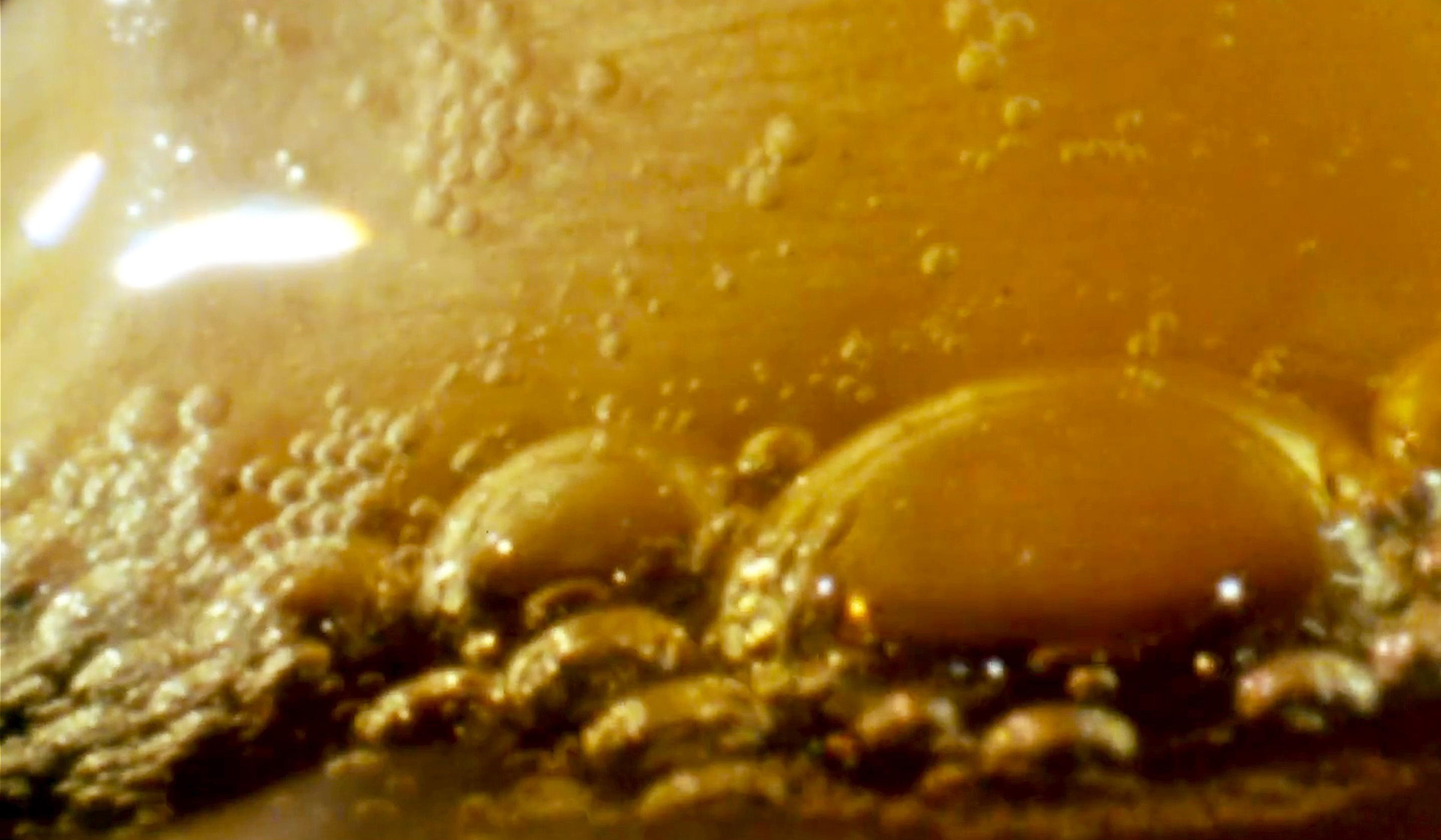 Close-up view of bubbling liquid of a golden brown colour with reflections of light on its surface.