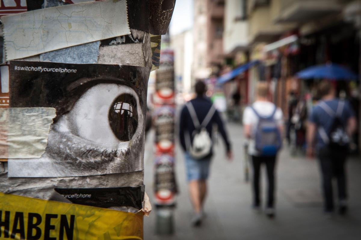 A street scene with blurry pedestrians in background and eye poster on post in foreground.