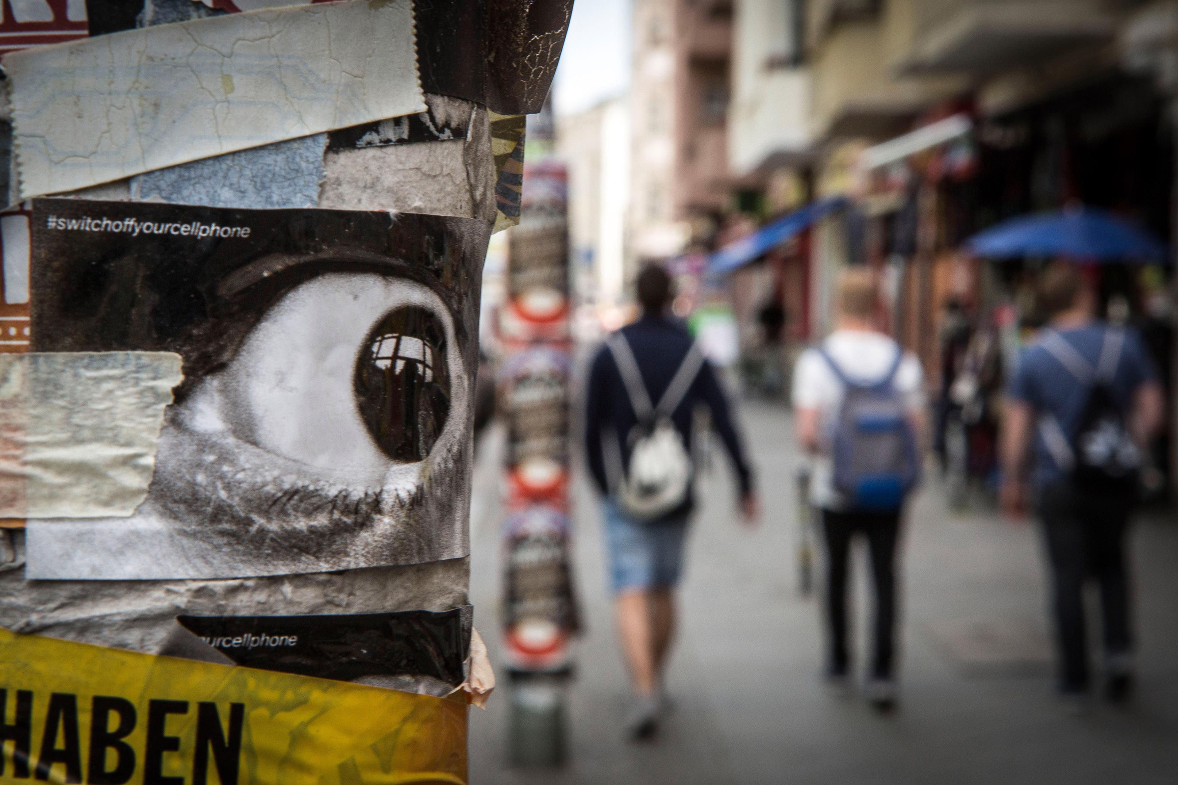 A street scene with blurry pedestrians in background and eye poster on post in foreground.