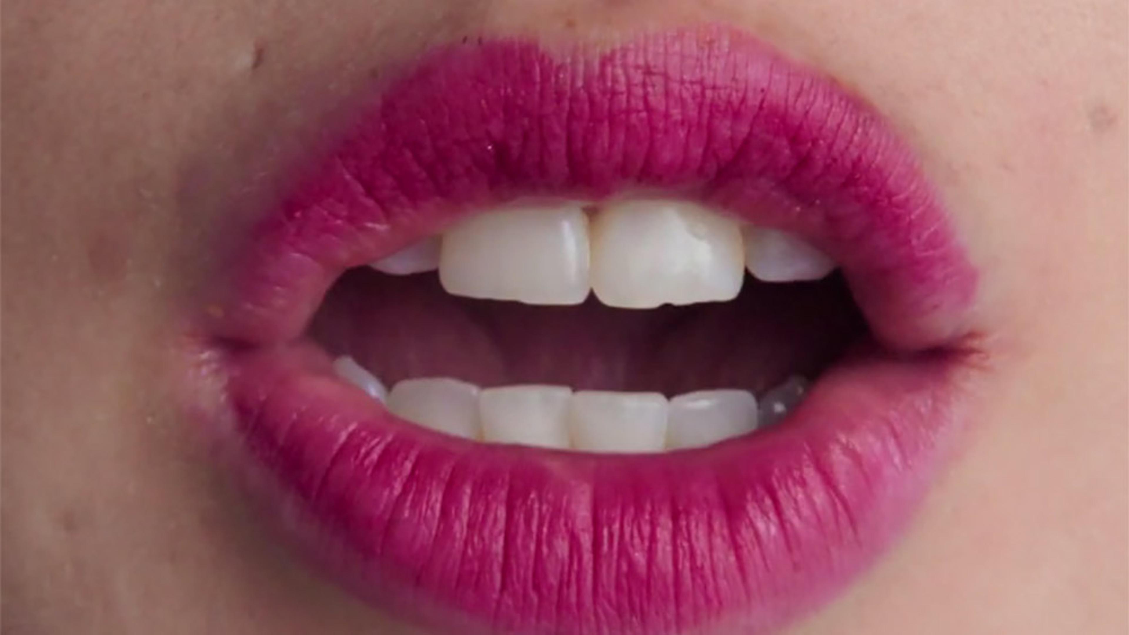 Close-up of lips with bright pink lipstick, slightly parted to show the brilliant white front teeth.