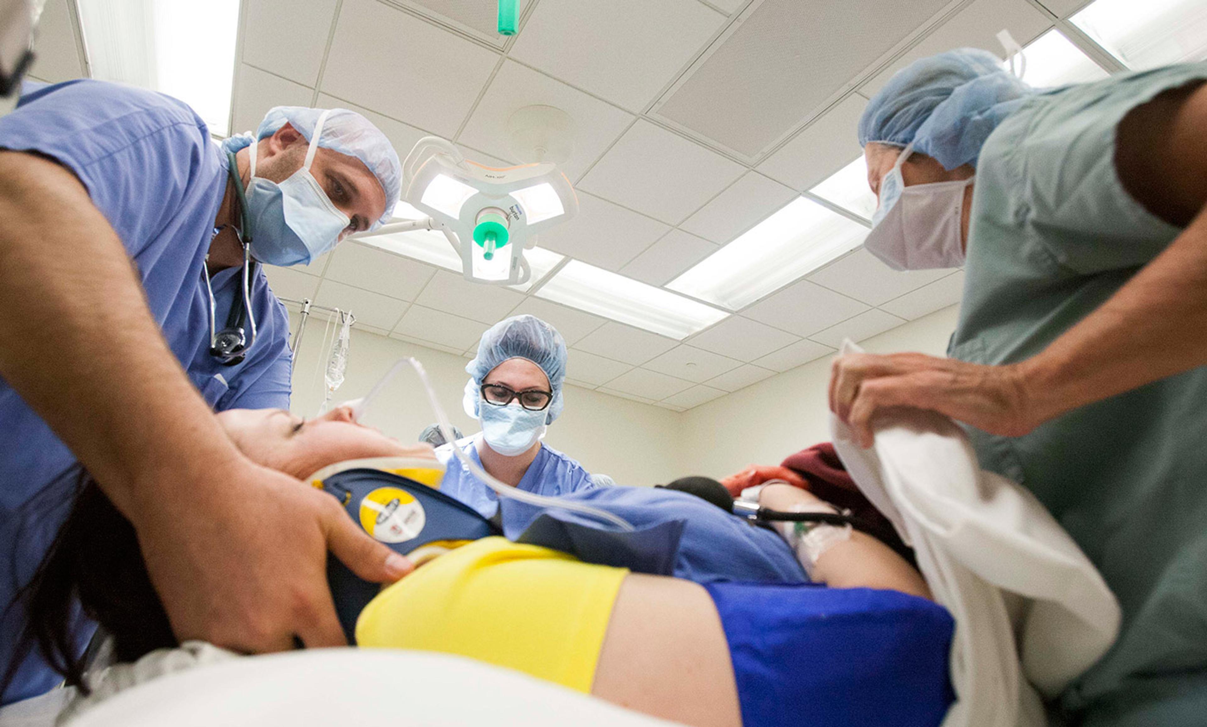 Three medical staff in surgical attire performing a procedure on a patient in an operating room with ceiling lights.