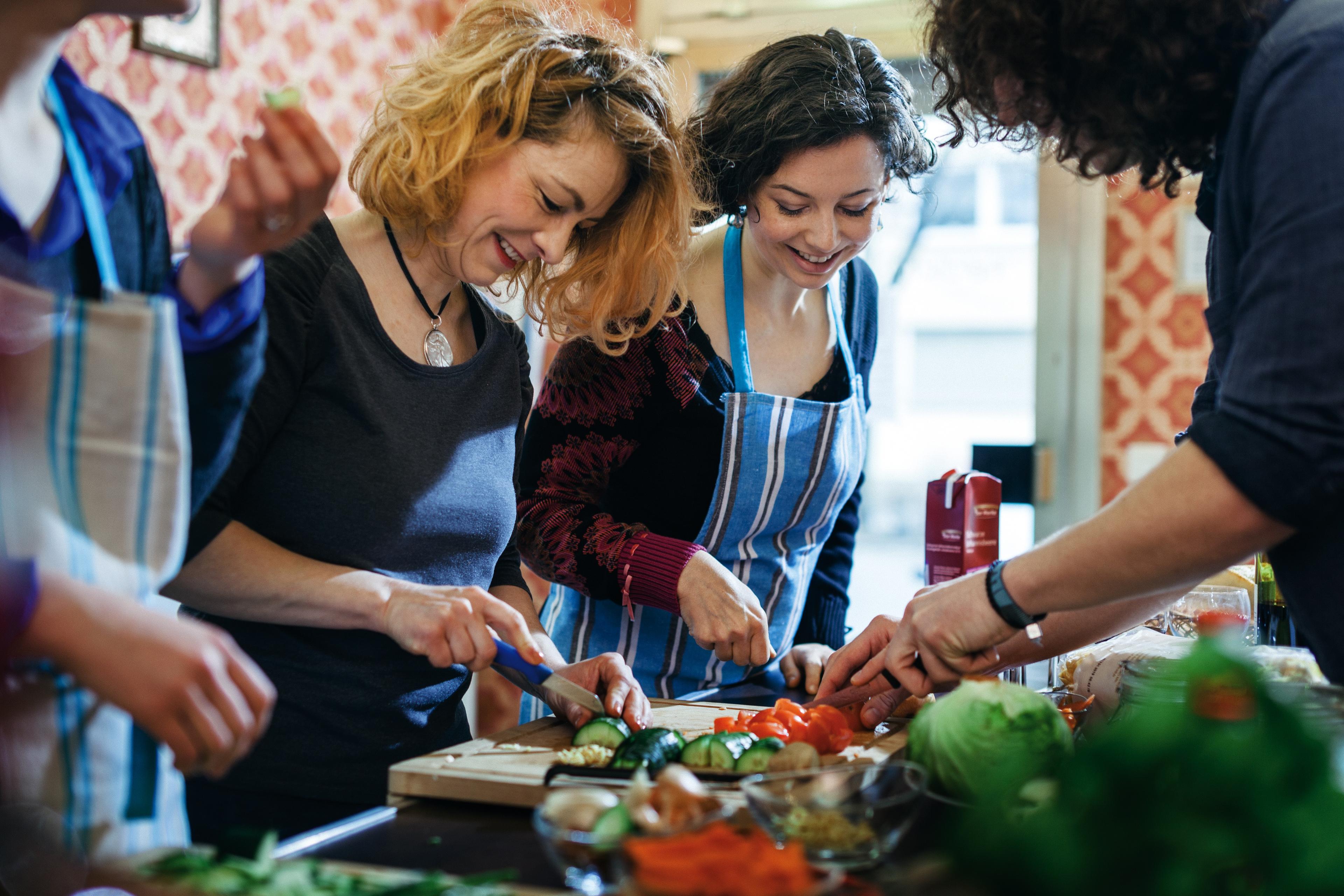 Photo of people in aprons smiling and chopping vegetables in a kitchen setting.
