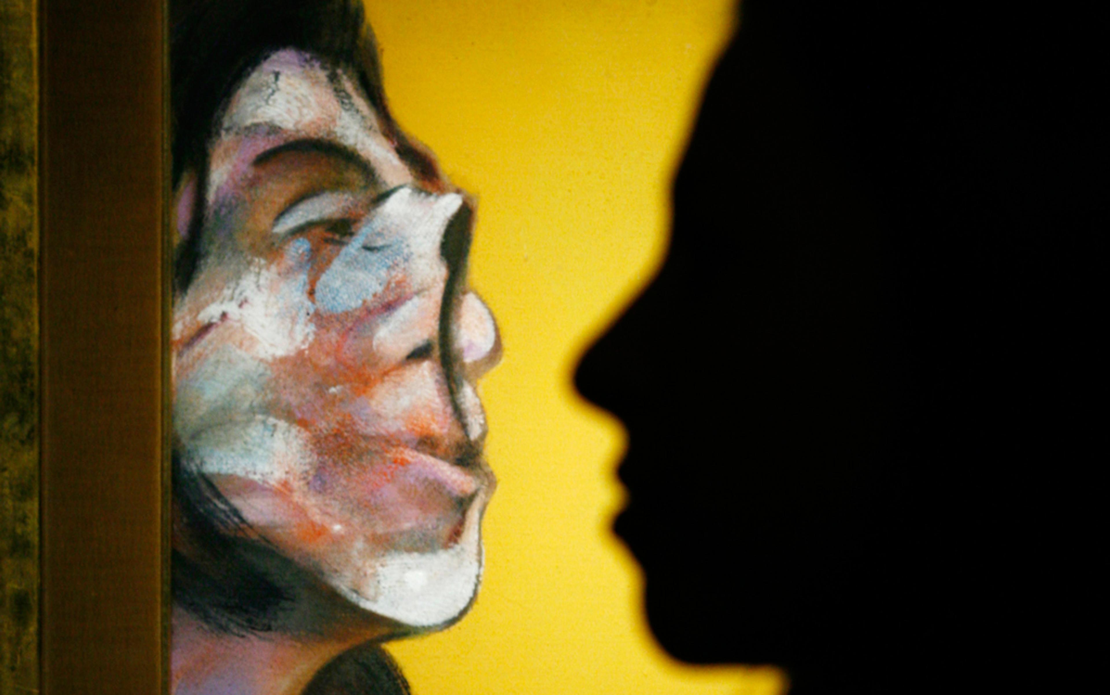 A silhouette of a person’s profile against a painted portrait of a face on a yellow background.