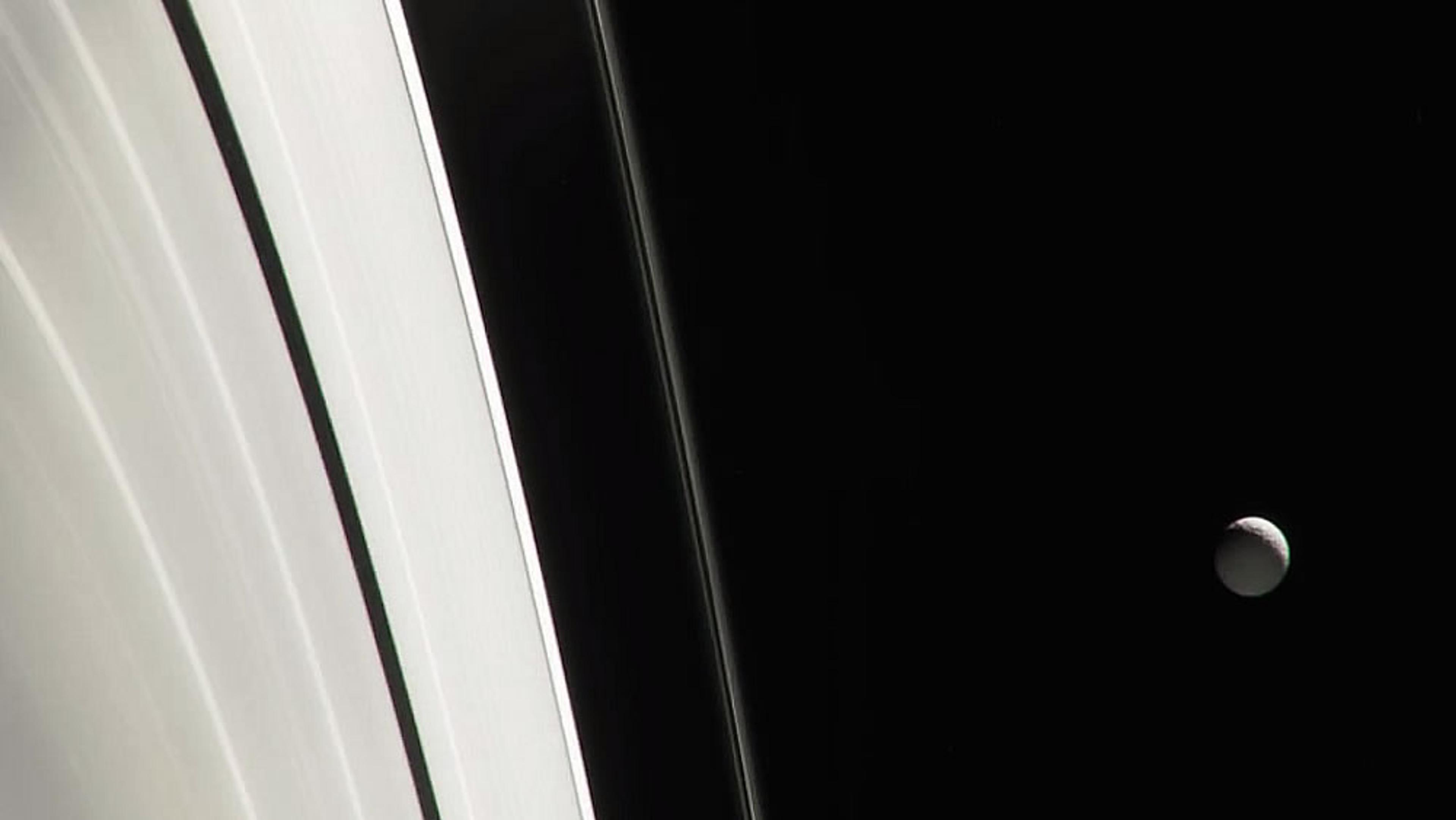 Saturn’s rings with a small moon visible in the blackness of space on the right, taken from a spacecraft.