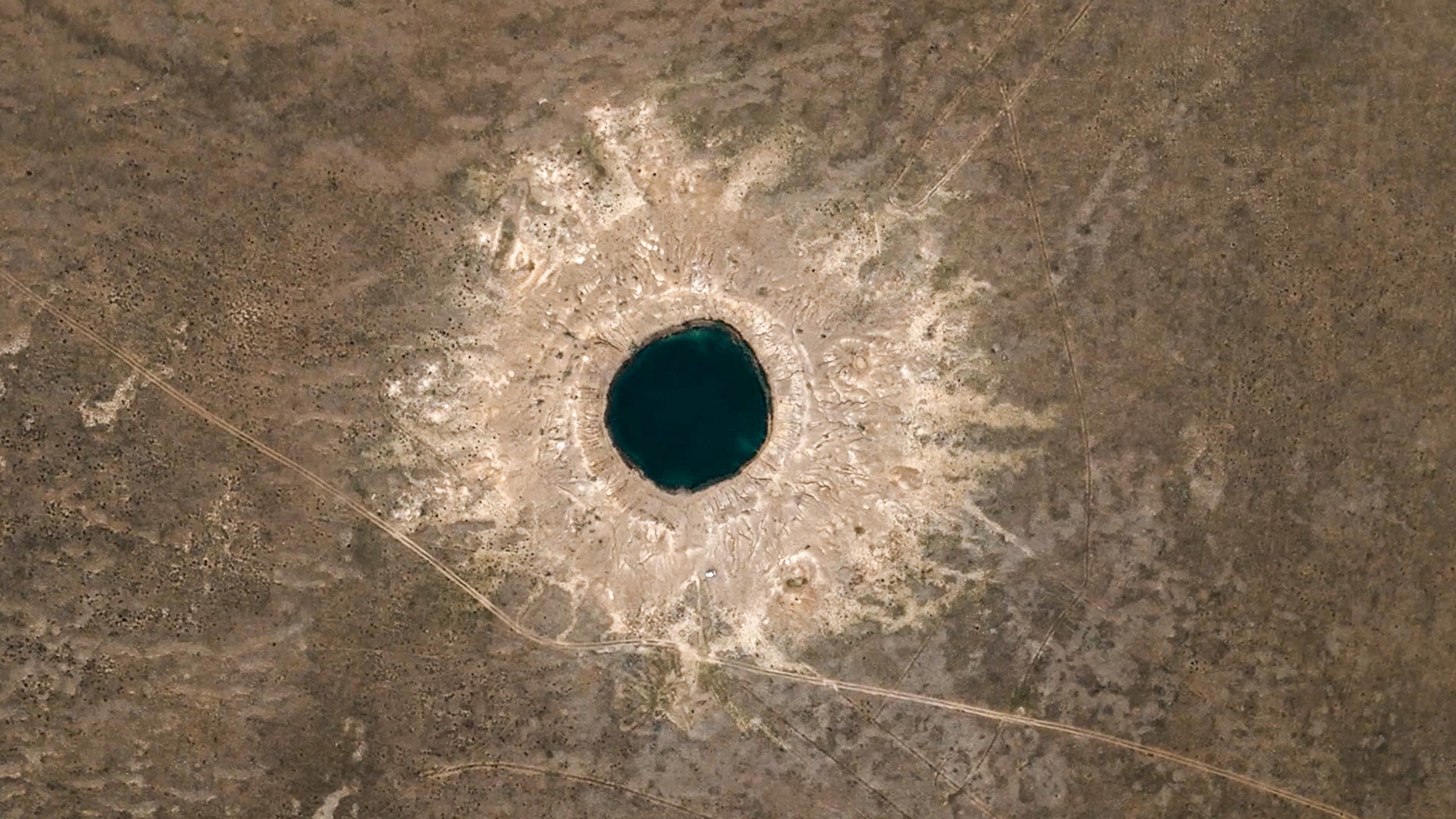 Aerial photo of a large circular crater with a dark centre in a brown landscape, resembling an impact site.