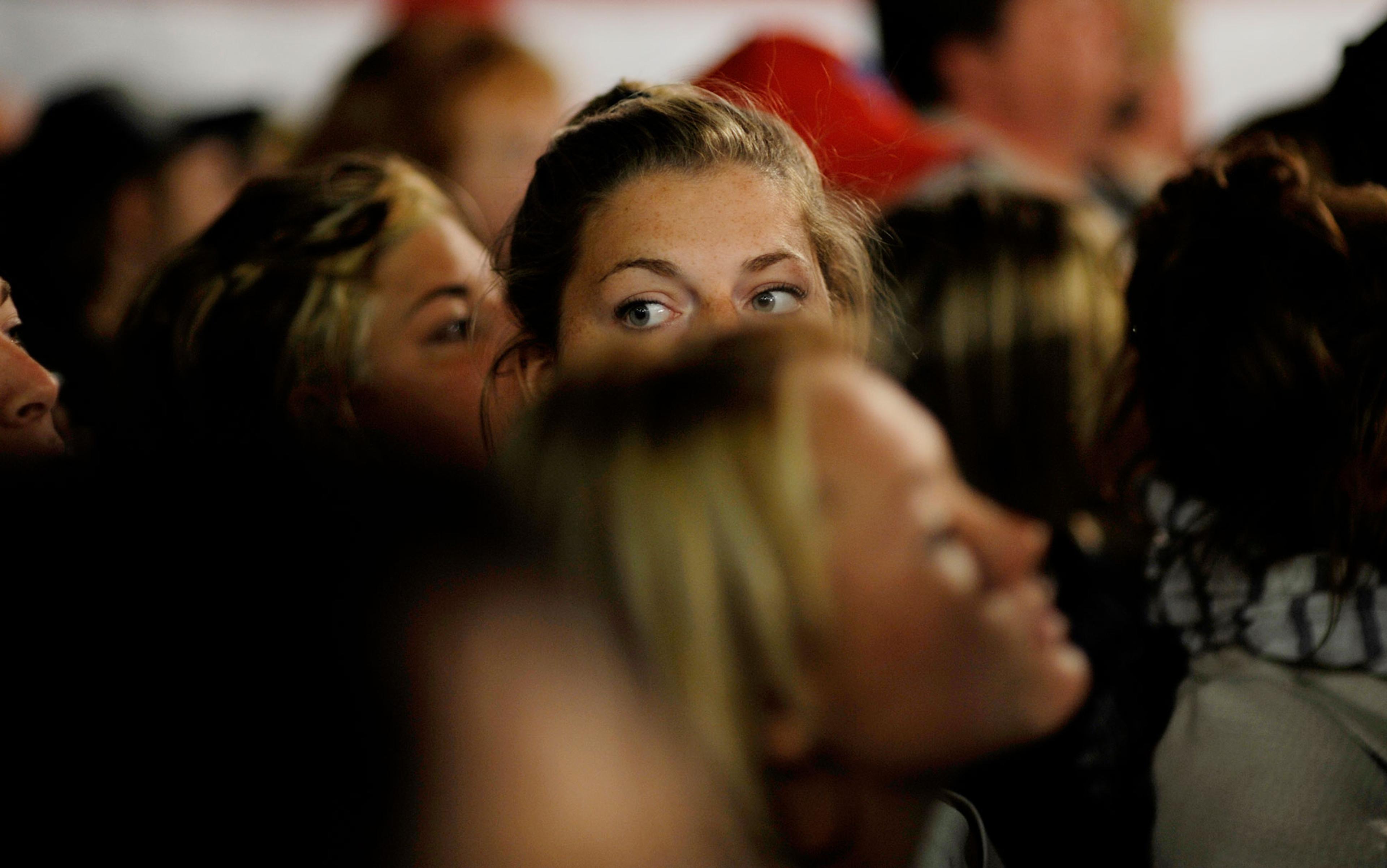 Photo of a crowd with a focused young woman looking to the side, surrounded by blurred faces in the foreground.