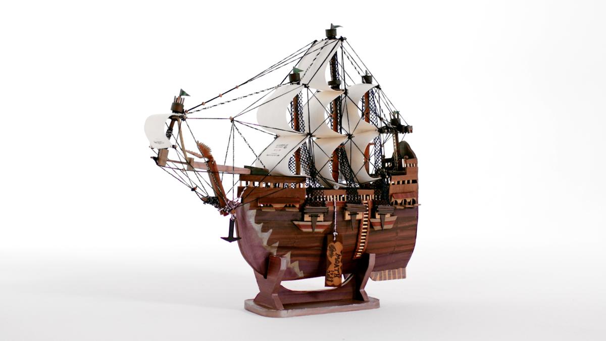 Wooden model of a sailing ship with multiple masts and detailed rigging on a white background.