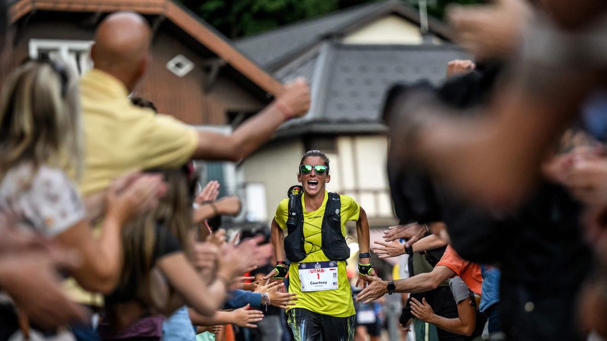 A smiling runner in a yellow shirt high-fiving a cheering crowd on a street lined with buildings and trees.