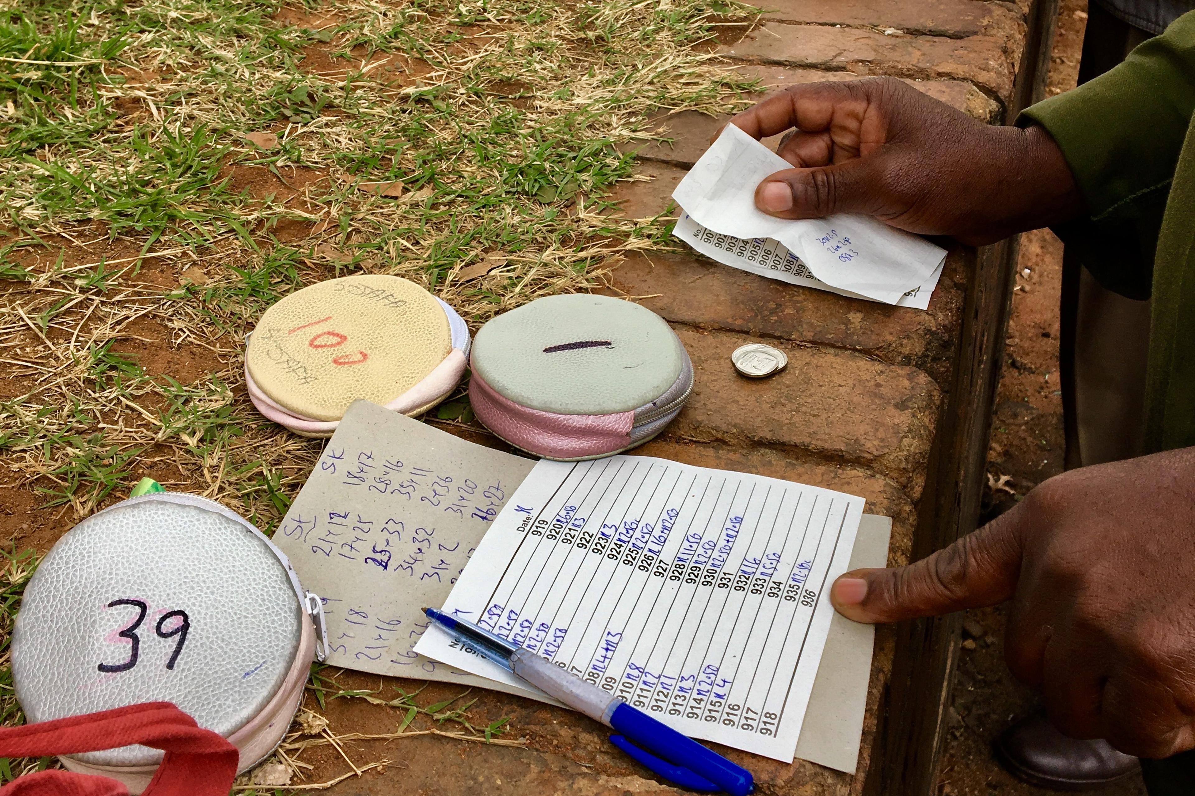 Photo of hands handling betting tokens, coins and paper slips on a brick surface with grass in background.