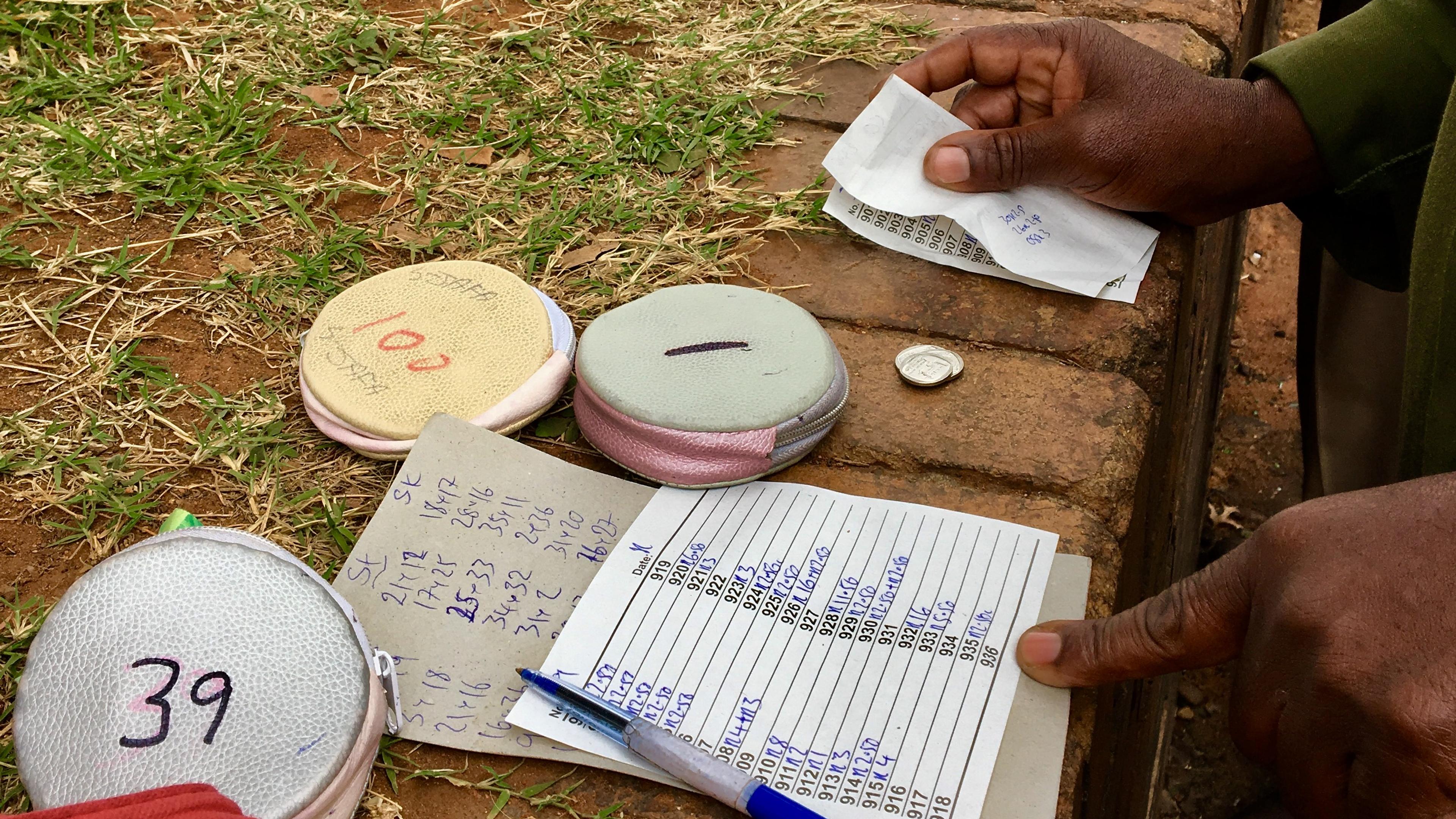 Photo of hands handling betting tokens, coins and paper slips on a brick surface with grass in background.