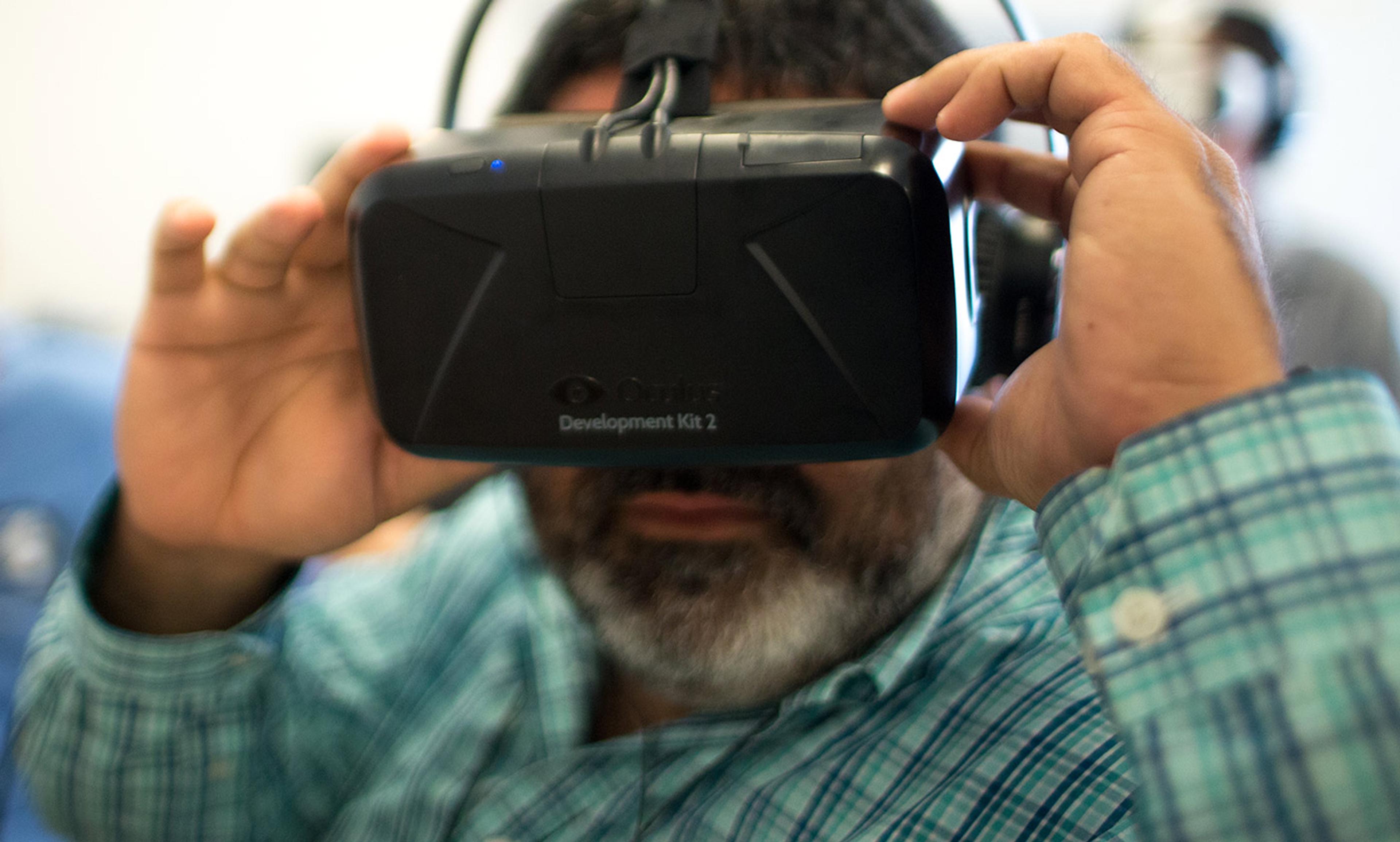 A person holding an Oculus Development Kit 2 VR headset to their eyes, wearing a blue plaid shirt.