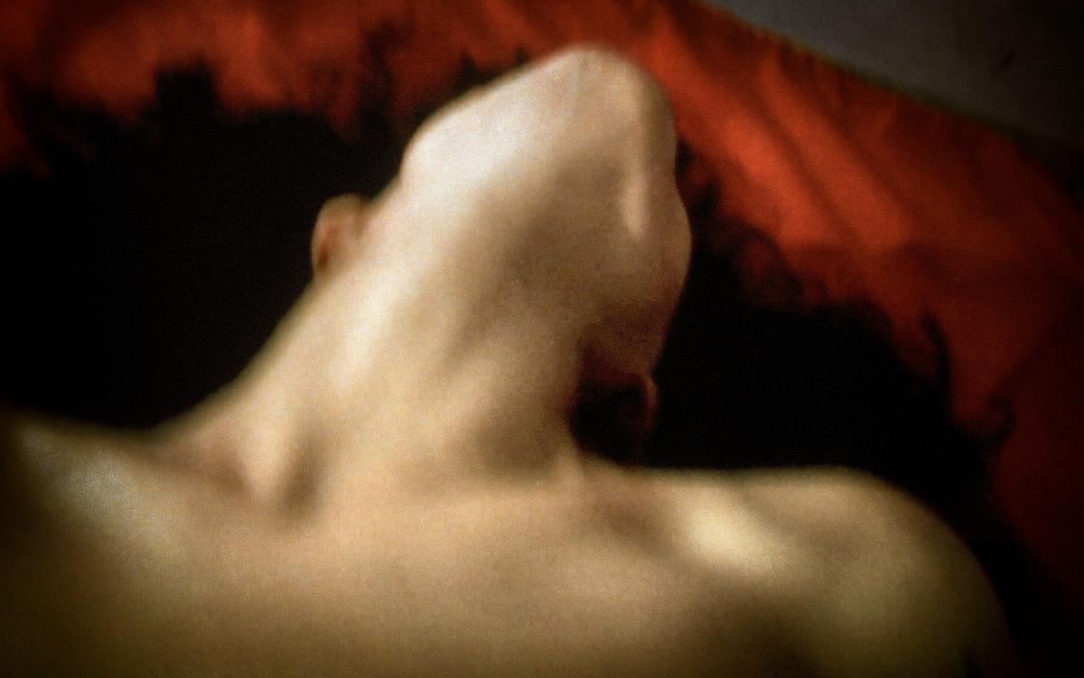 Blurry photo of a person lying back with head tilted, set against a red and dark background.