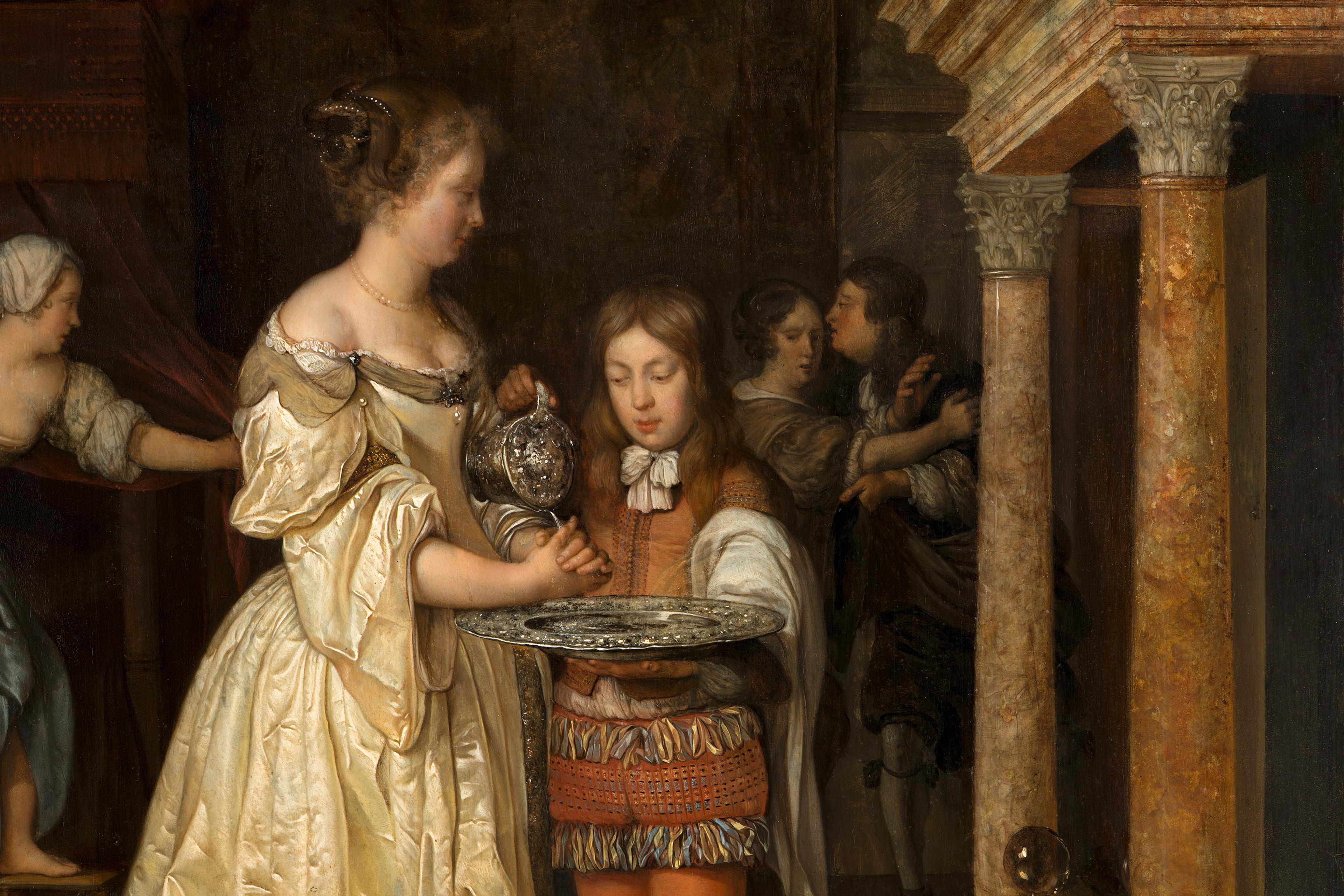 Woman in historical dress washing her hands with water poured by a child from a jug, with onlookers in an ornate interior setting.