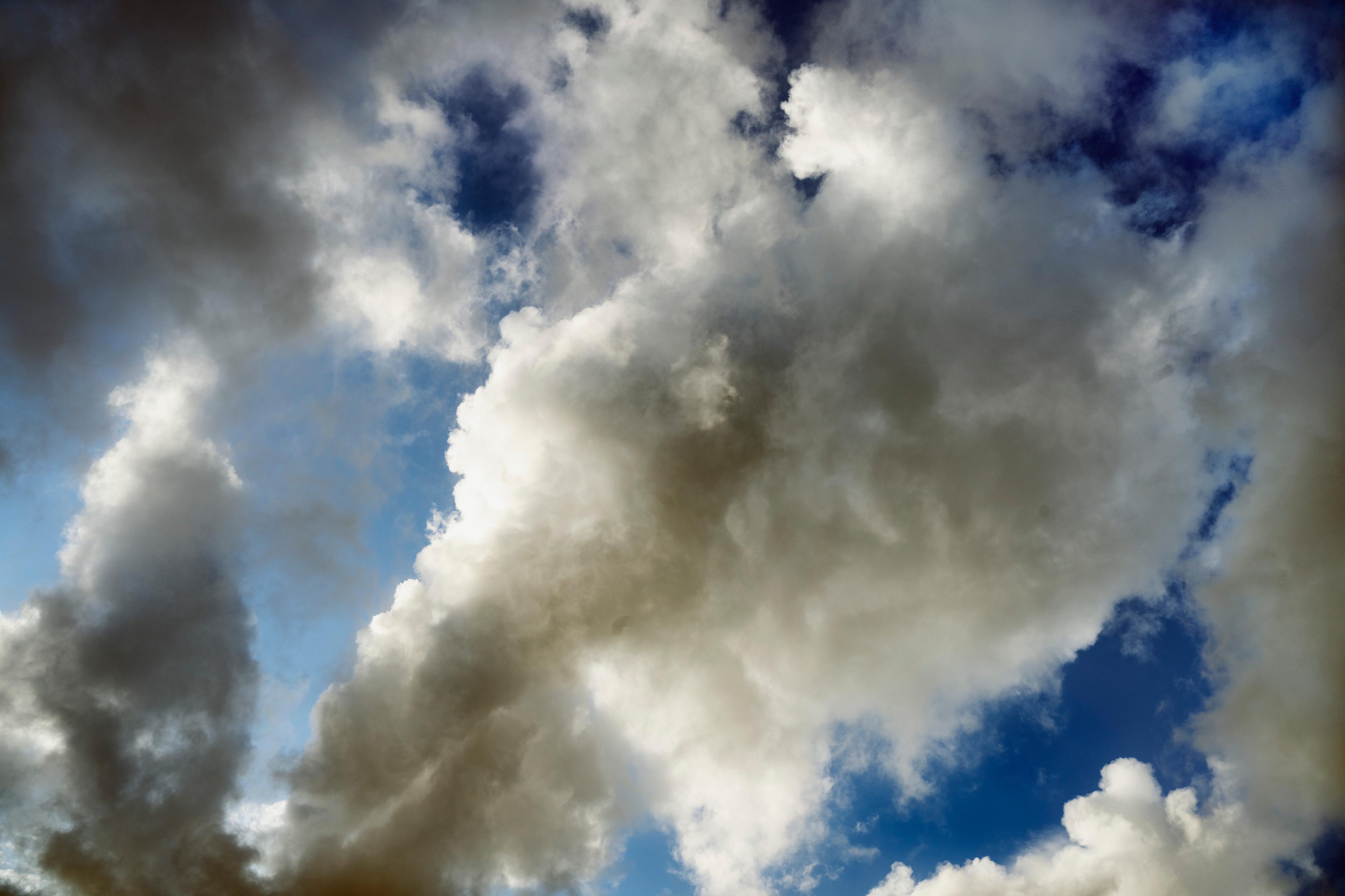 Photo of a cloudy sky with large white and grey clouds against a backdrop of blue sky.