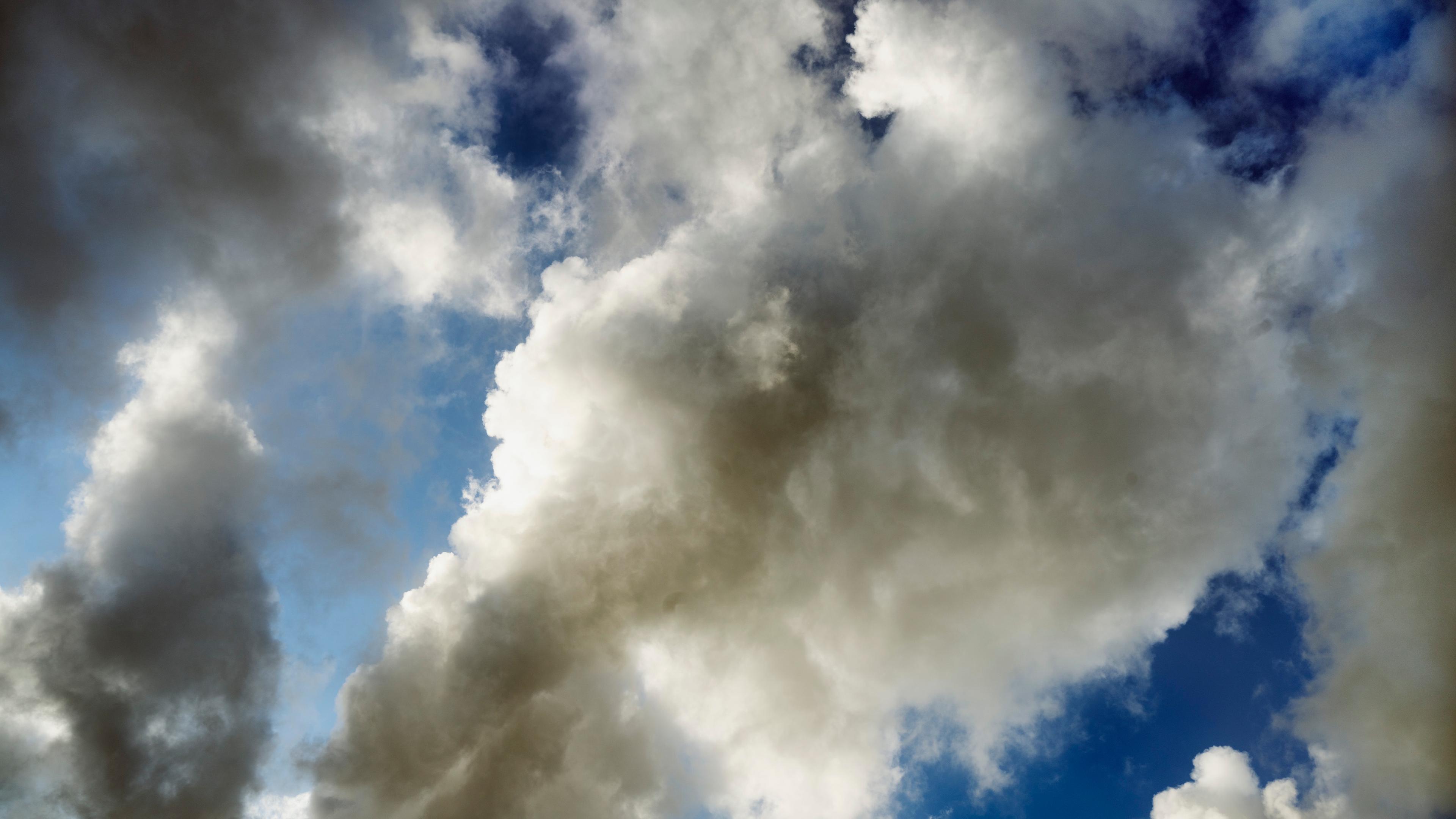 Photo of a cloudy sky with large white and grey clouds against a backdrop of blue sky.