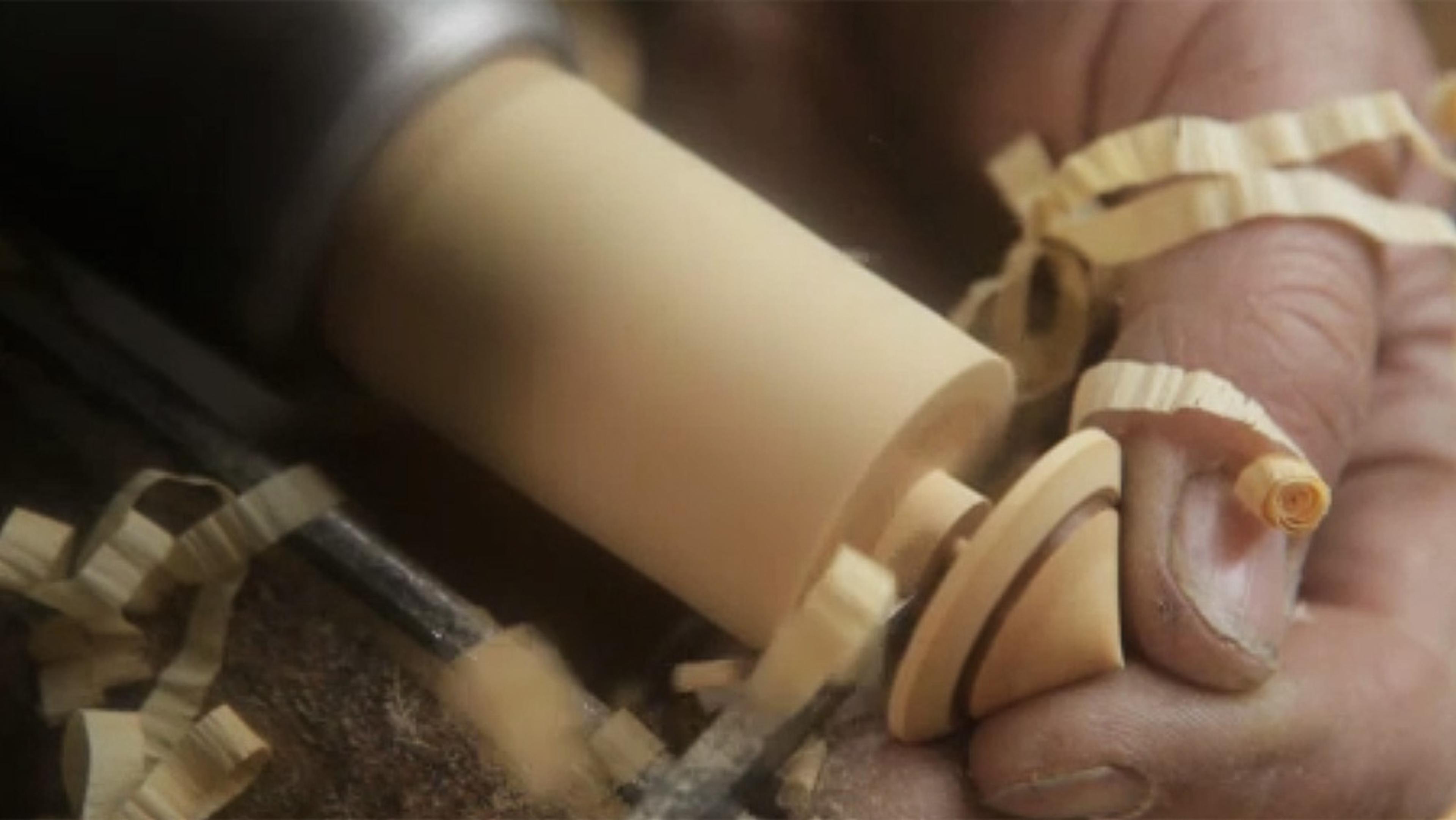 Someone carving wood with a tool, creating thin shavings. The person is holding the wood securely while working.