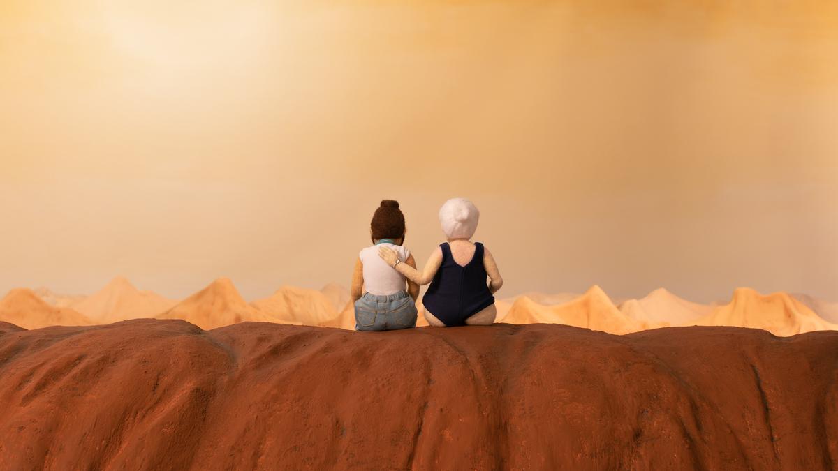 Two felt figures sit together facing a desert landscape under a warm sky.