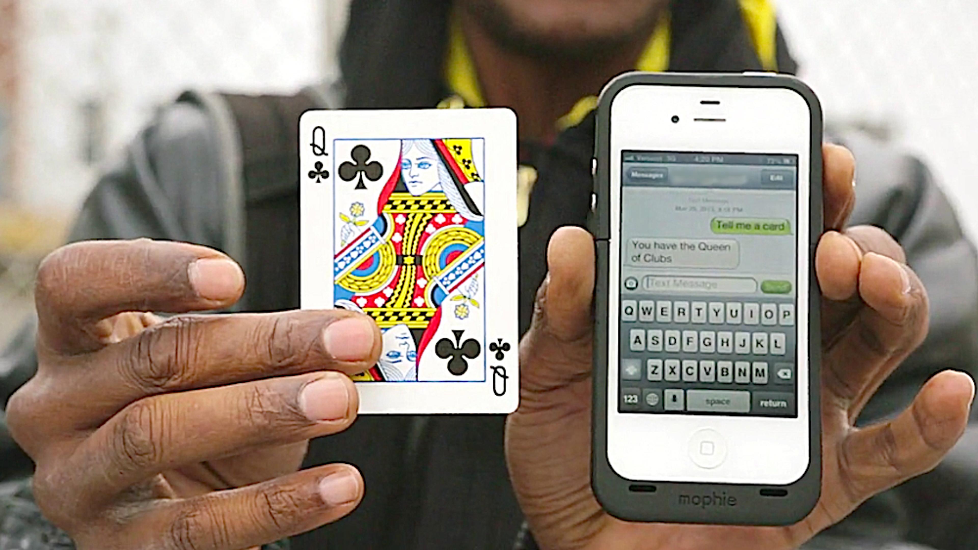 A person holding the Queen of Clubs playing card in one hand and a smartphone in the other displaying a related text message.