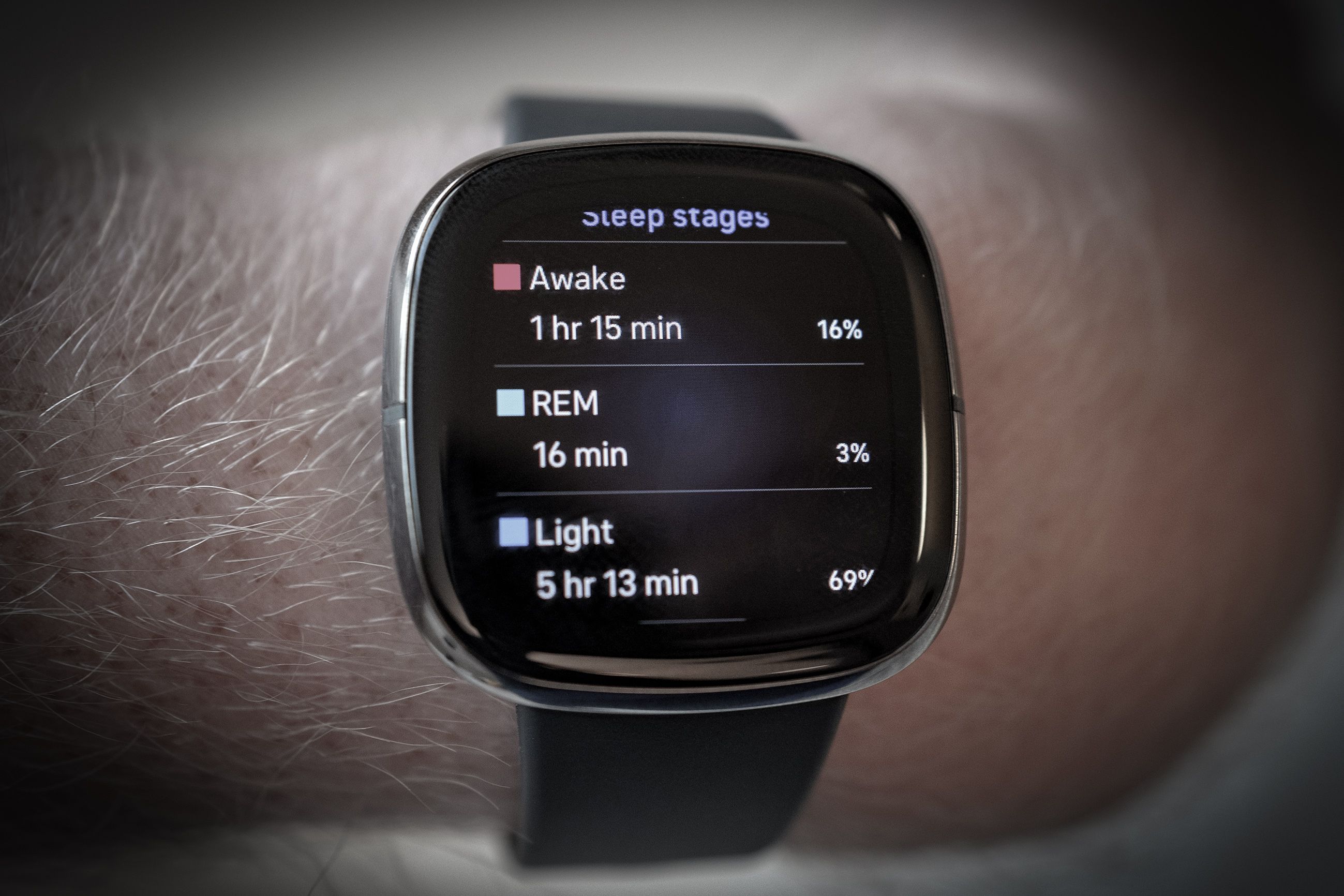 A smartwatch displaying sleep stages: Awake 1hr 15min, REM 16min, Light 5hr 13min. It is worn on a wrist.