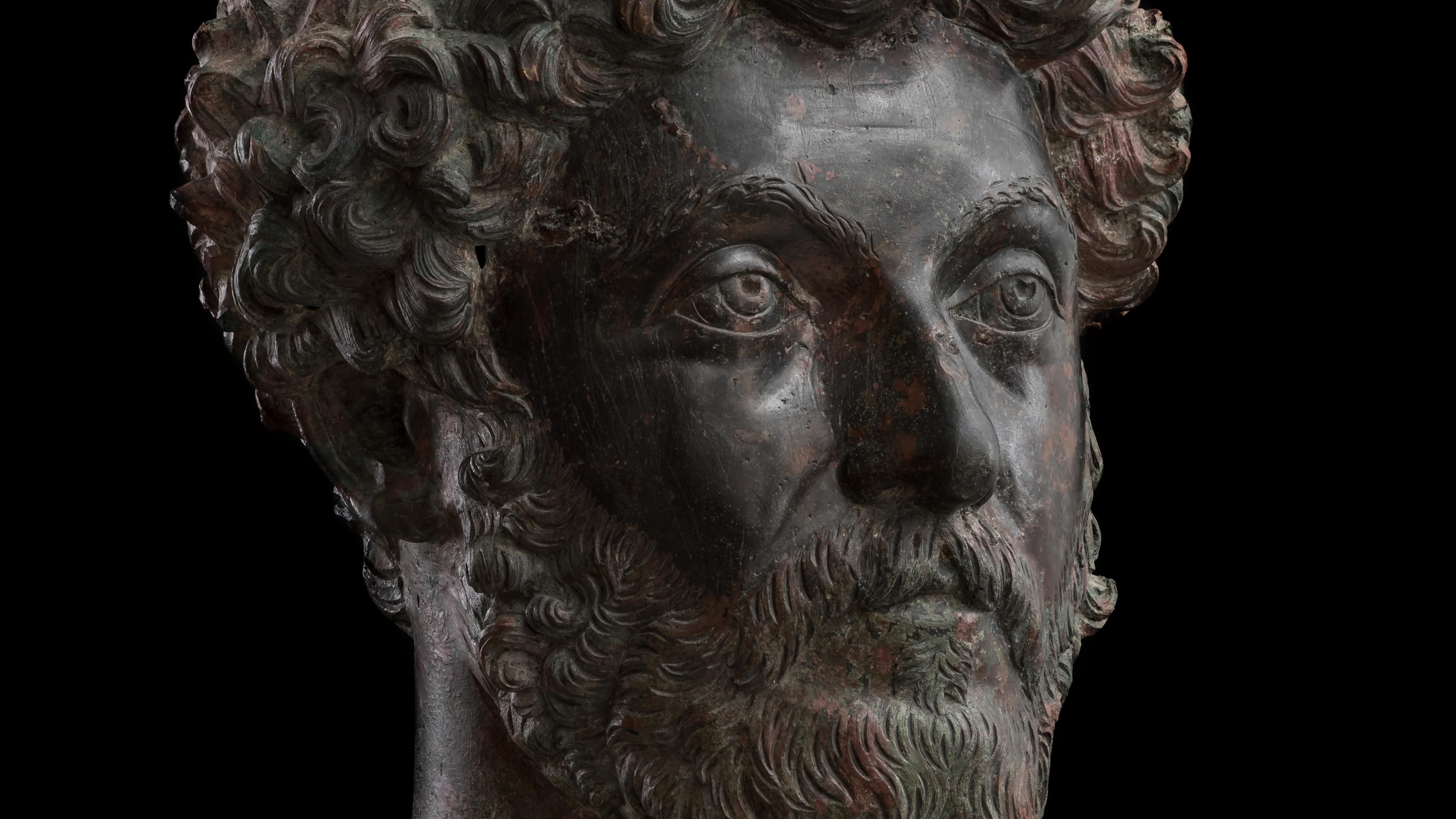 Bronze statue head with curly hair and beard on black background, depicting a solemn expression, sculpture.