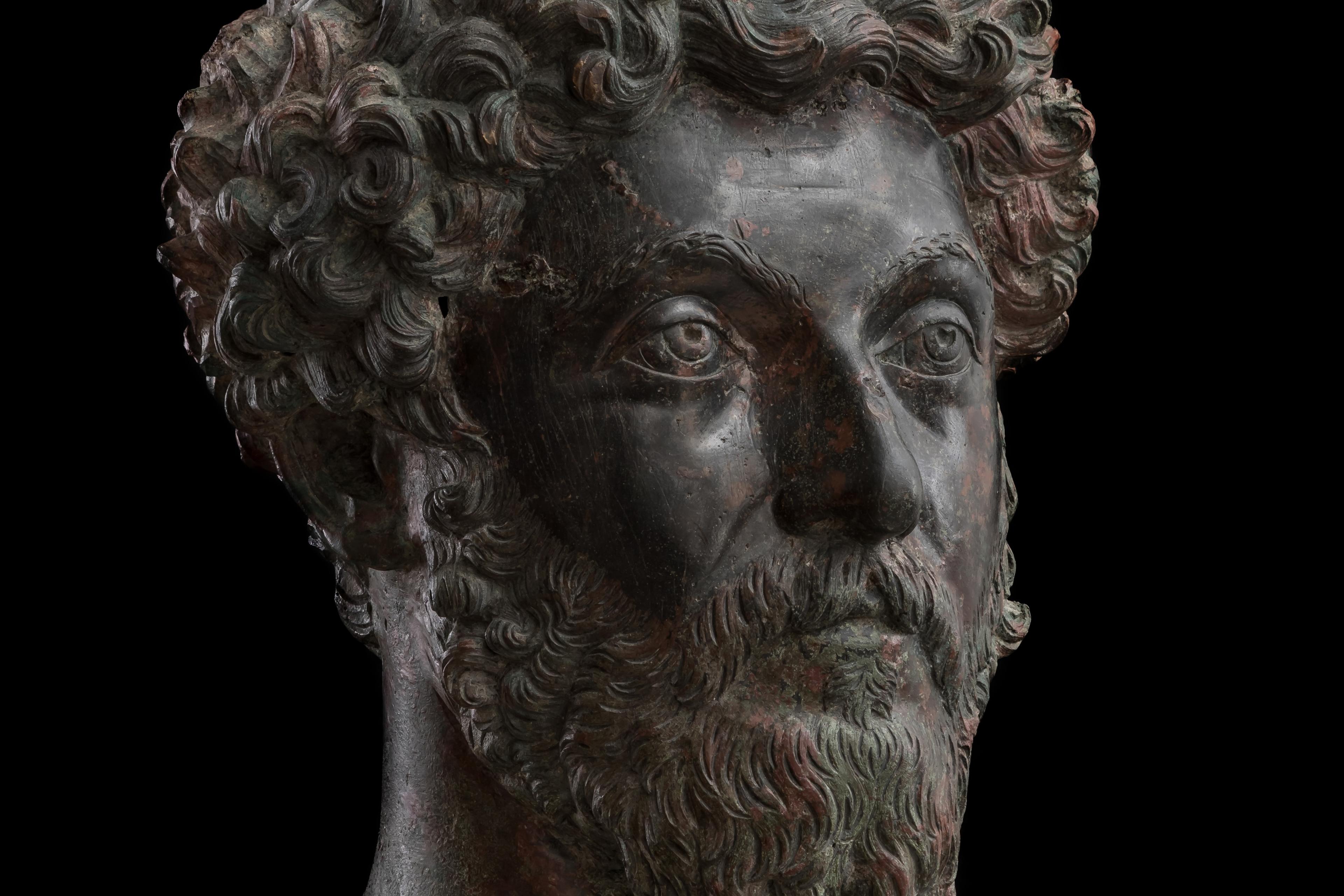 Bronze statue head with curly hair and beard on black background, depicting a solemn expression, sculpture.
