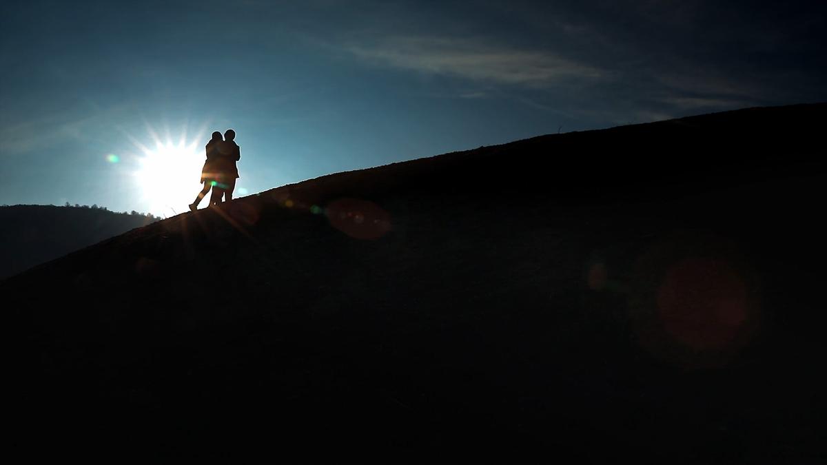 Photo of two people silhouetted on a hilltop against the sunset, creating a warm glow with a clear blue sky above.