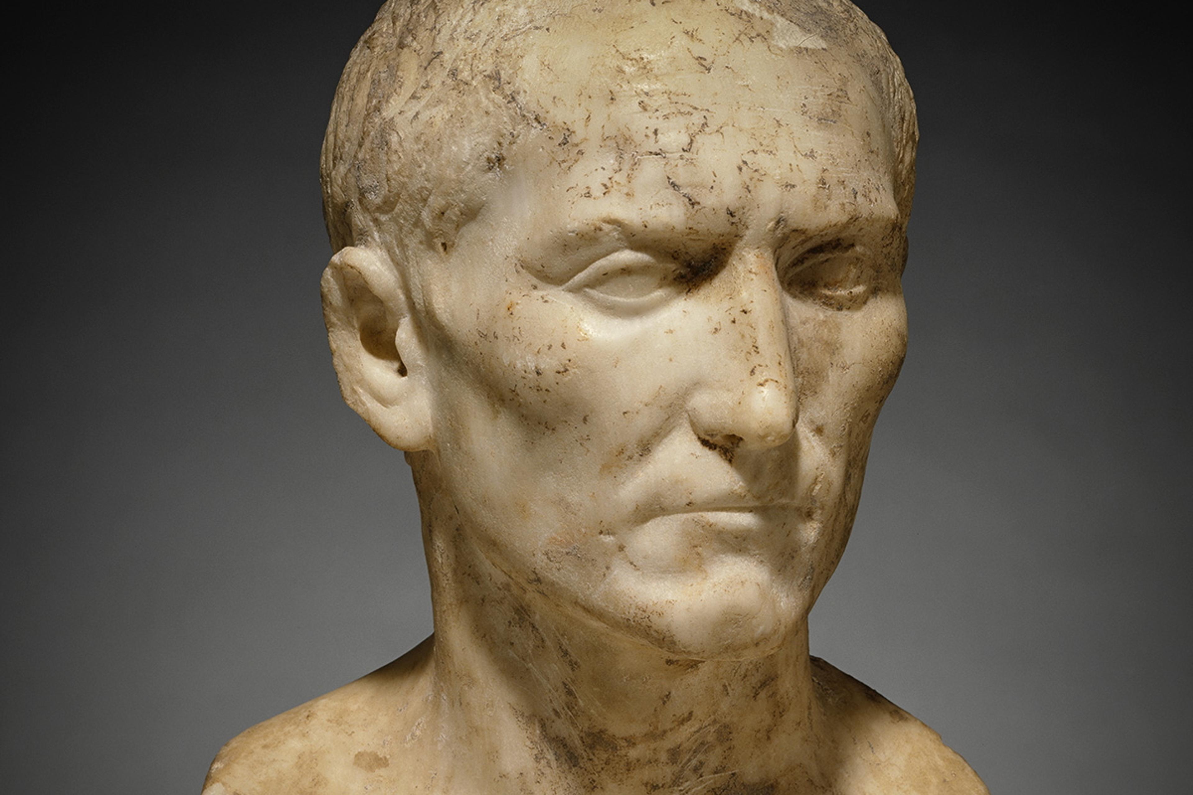 Marble bust of a man with a solemn expression, Roman style, displayed against a dark background.