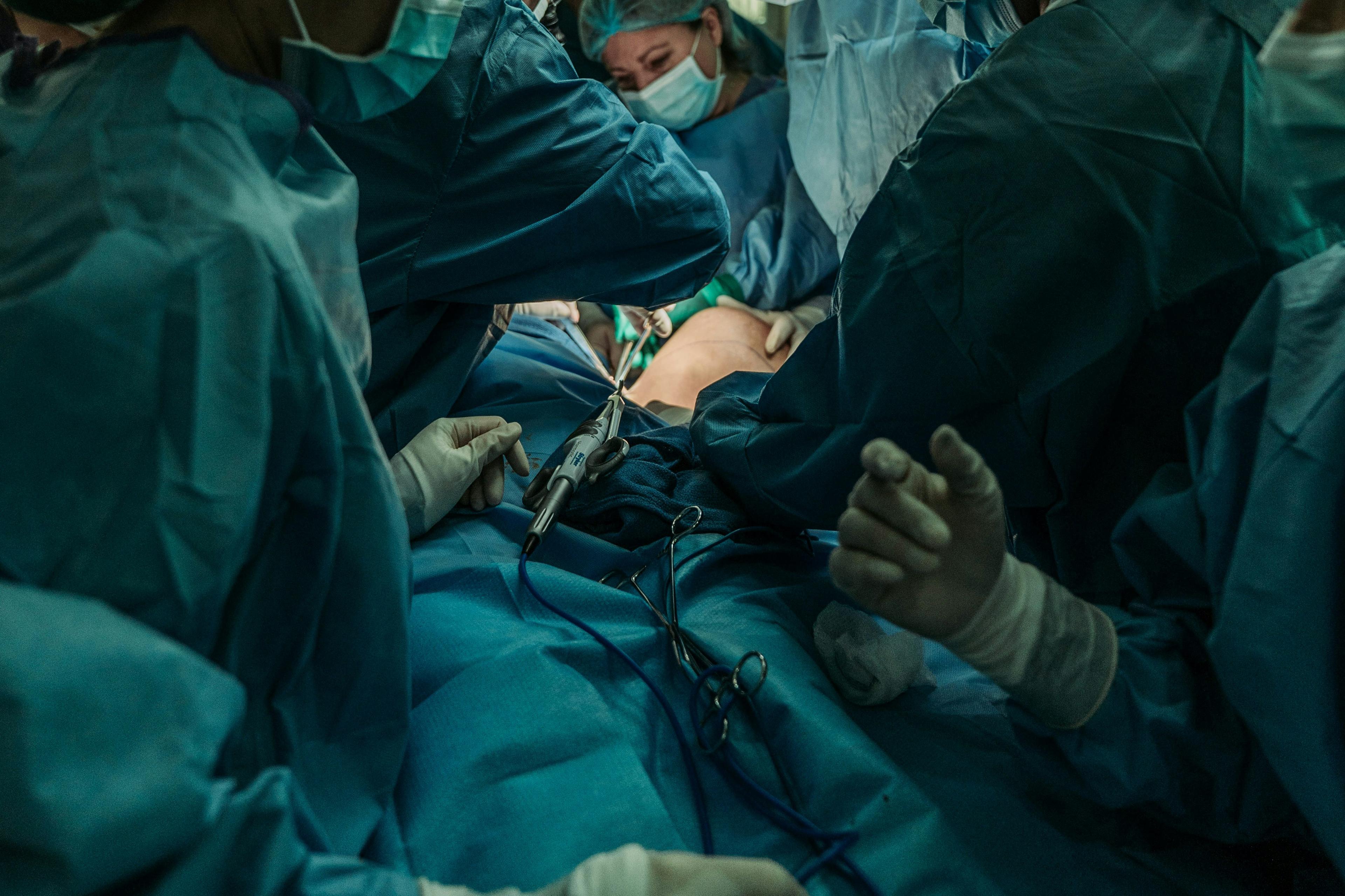 Surgeons in blue attire performing an operation in a theatre, with medical tools visible.