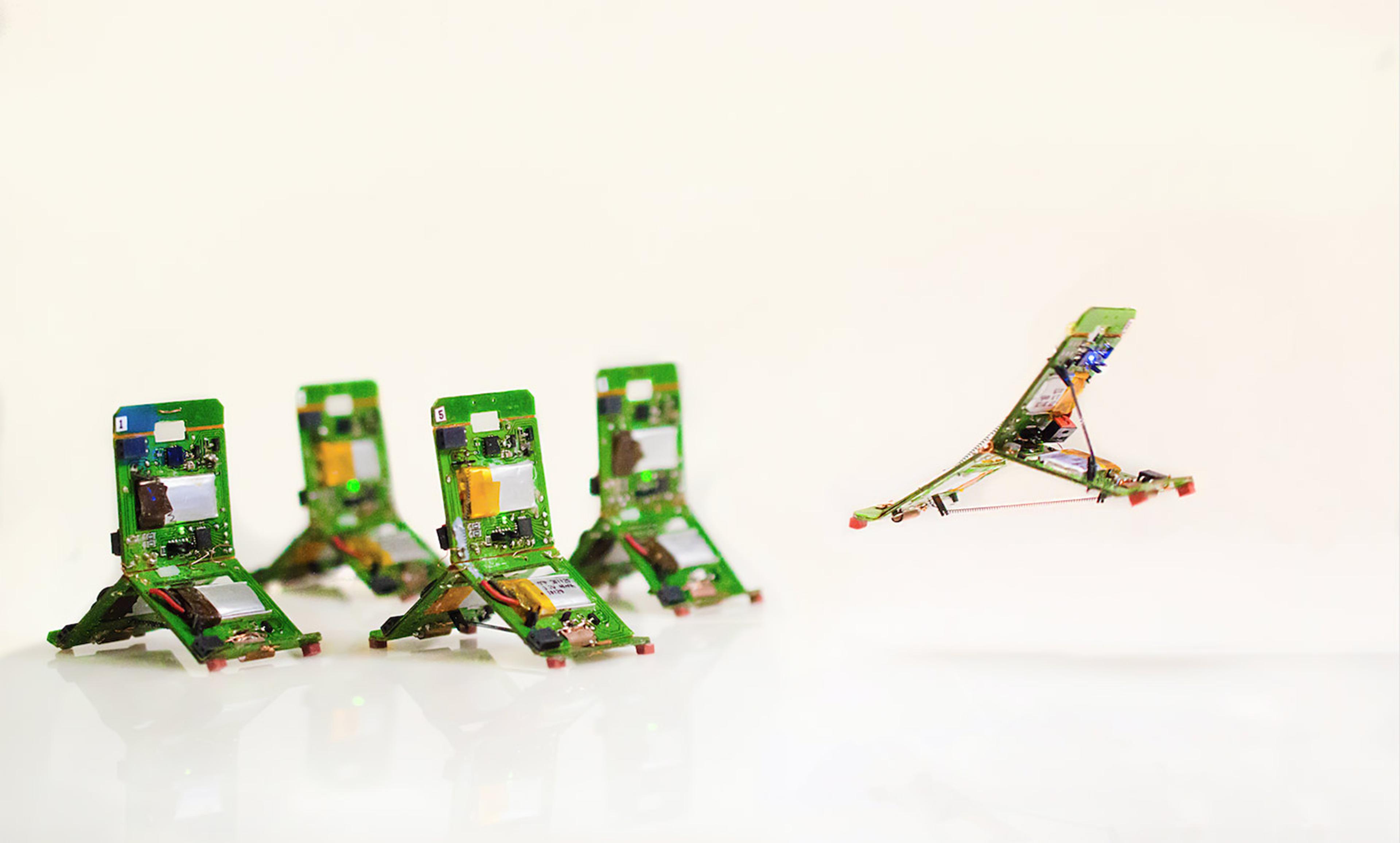 Four small green robot units on a white surface with one in mid-air, showcasing their ability to jump or move.