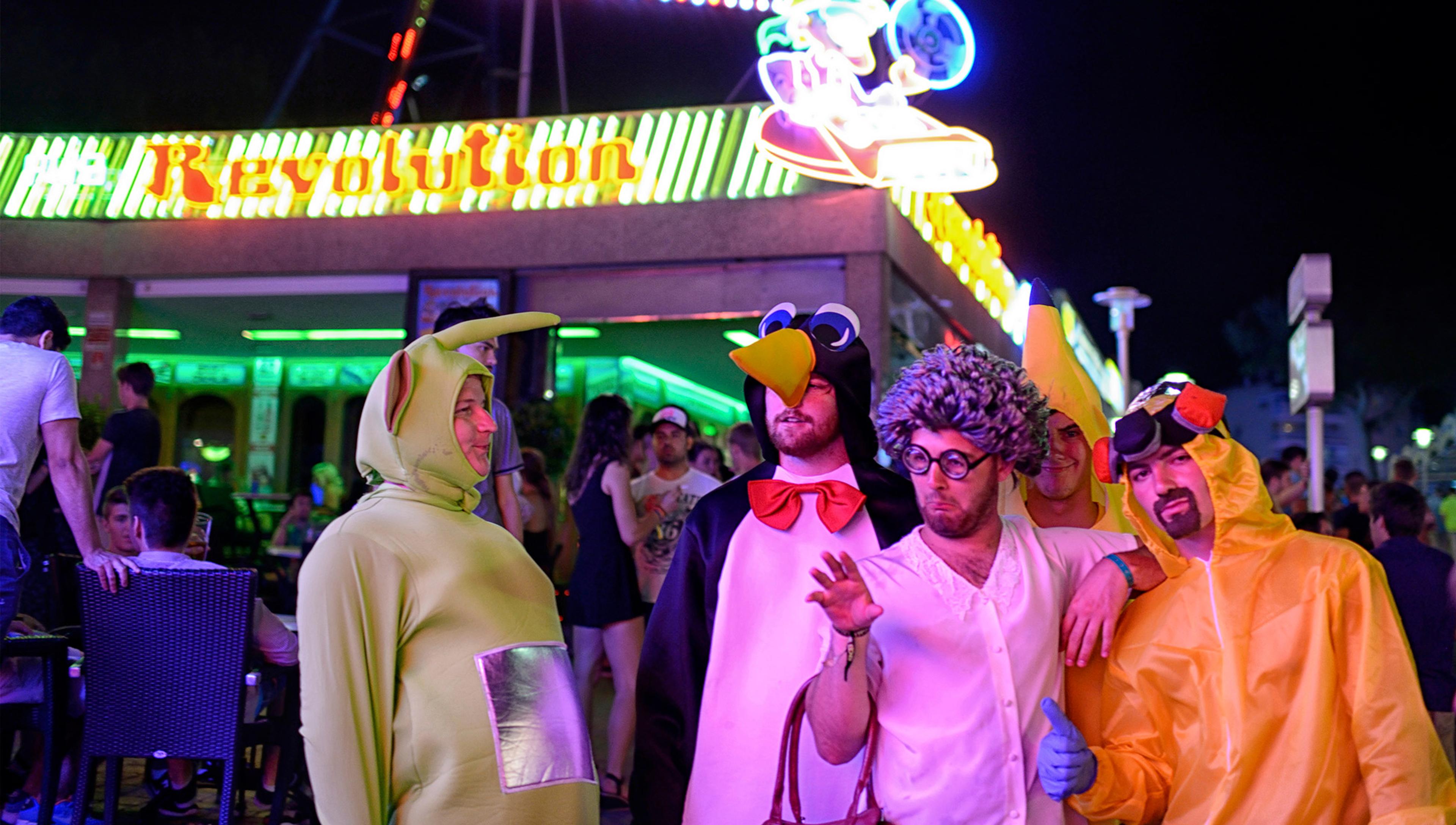 four men in strange fancy dress costumes stand in a fairground at night