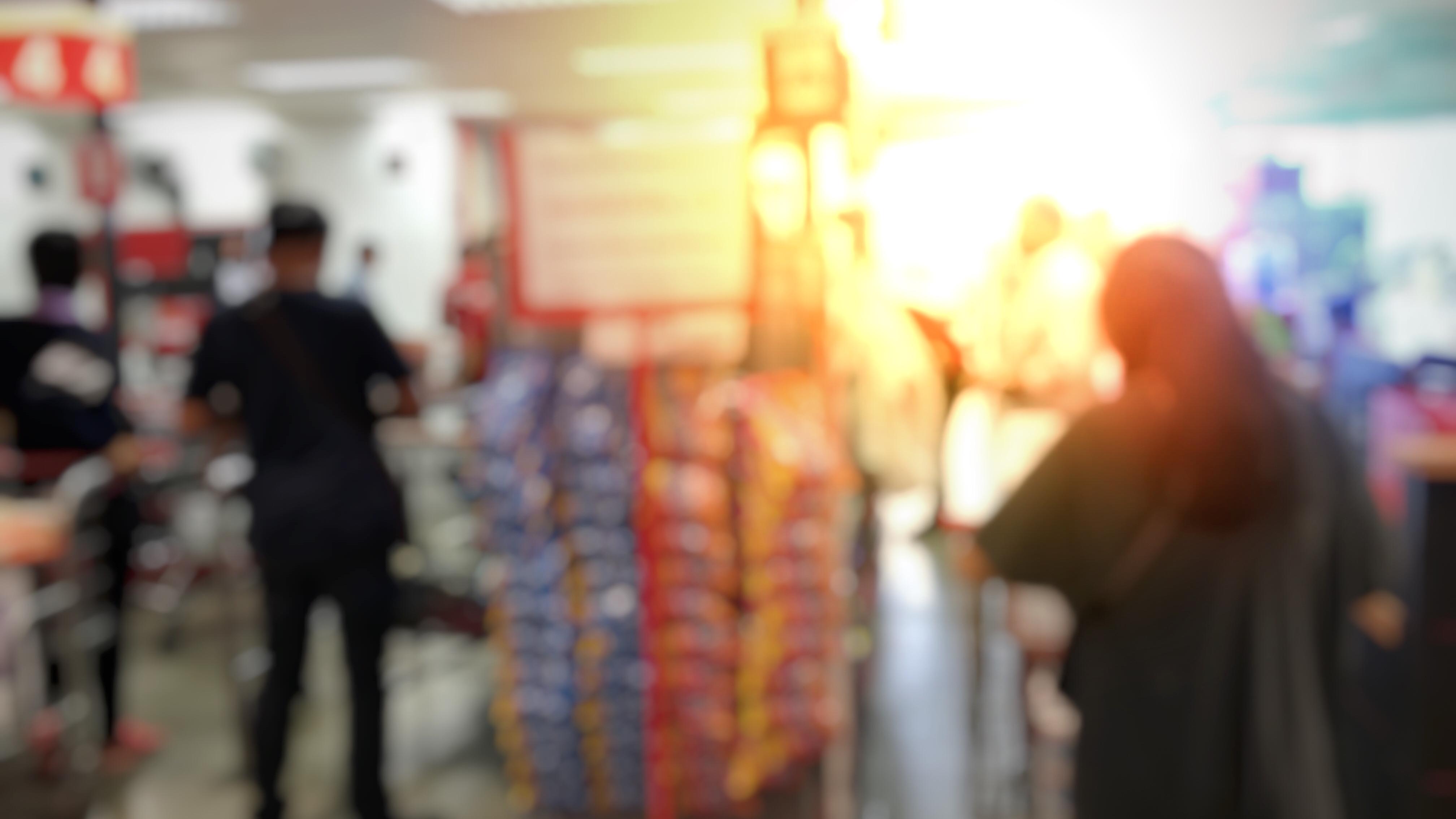 Blurry photo of a supermarket interior with people shopping, bright lighting and shelves filled with products.
