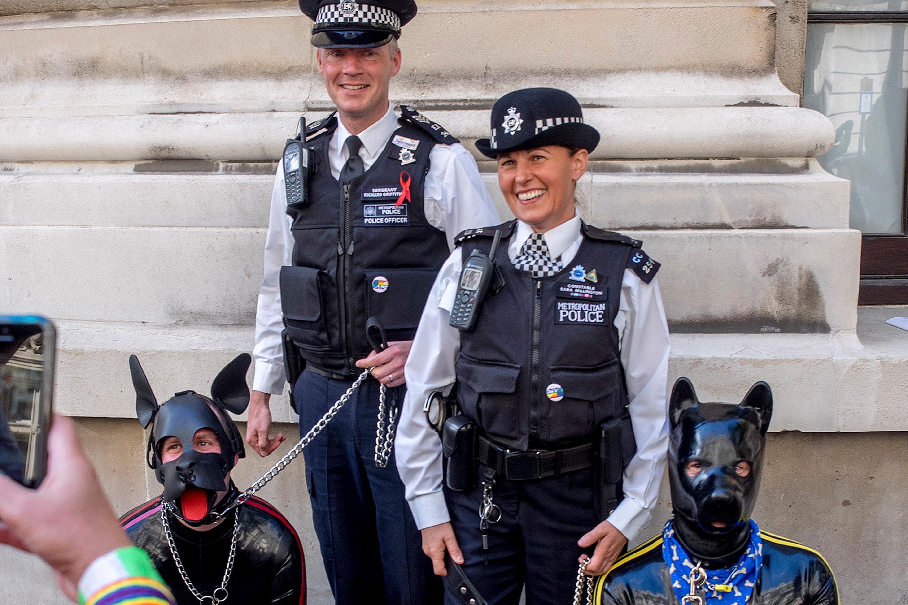 Photo of two police officers smiling next to two people in dog costumes, with one person capturing the moment on a phone.
