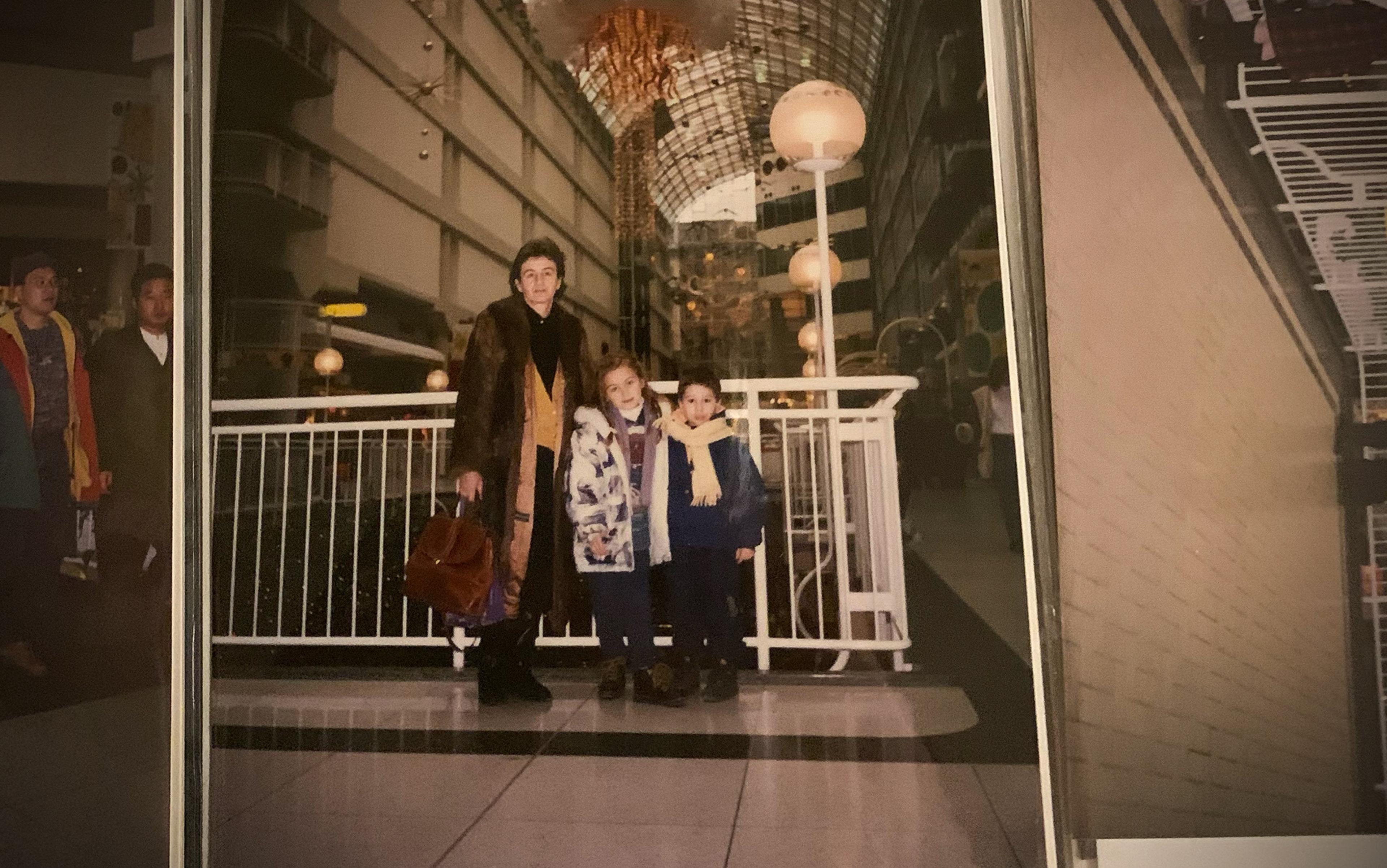 An adult and two children in a mall atrium, dressed in winter clothing.