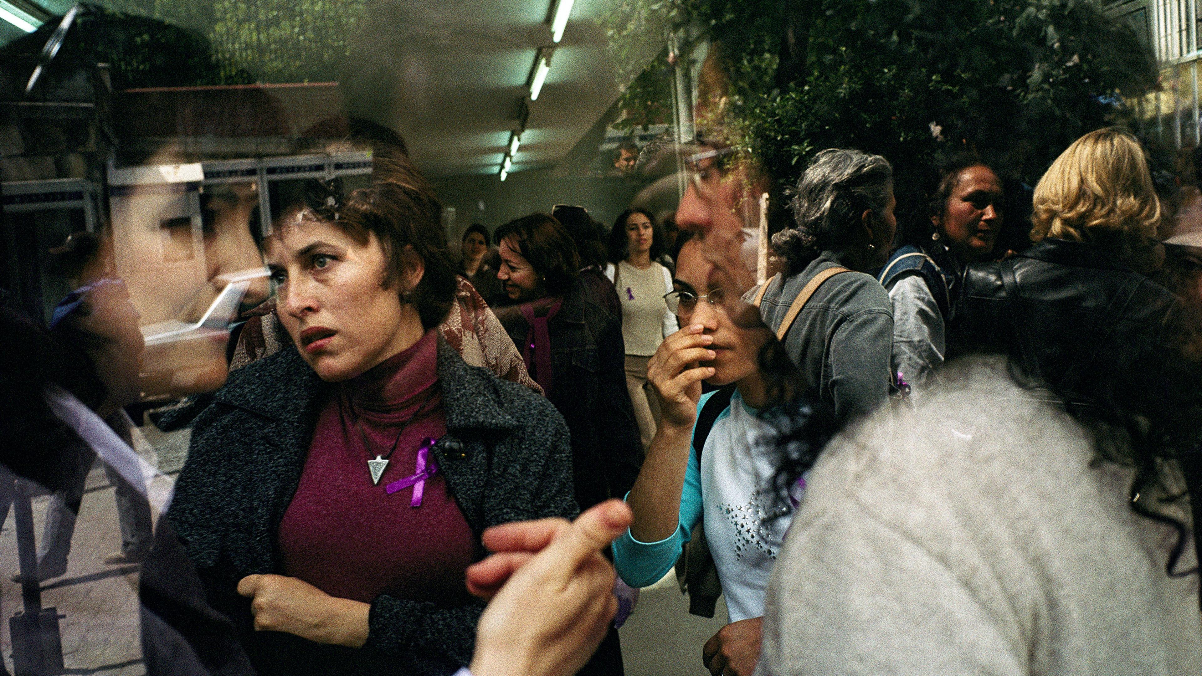 A group of people shown through reflective surfaces creating a layered effect, one wears a purple ribbon.