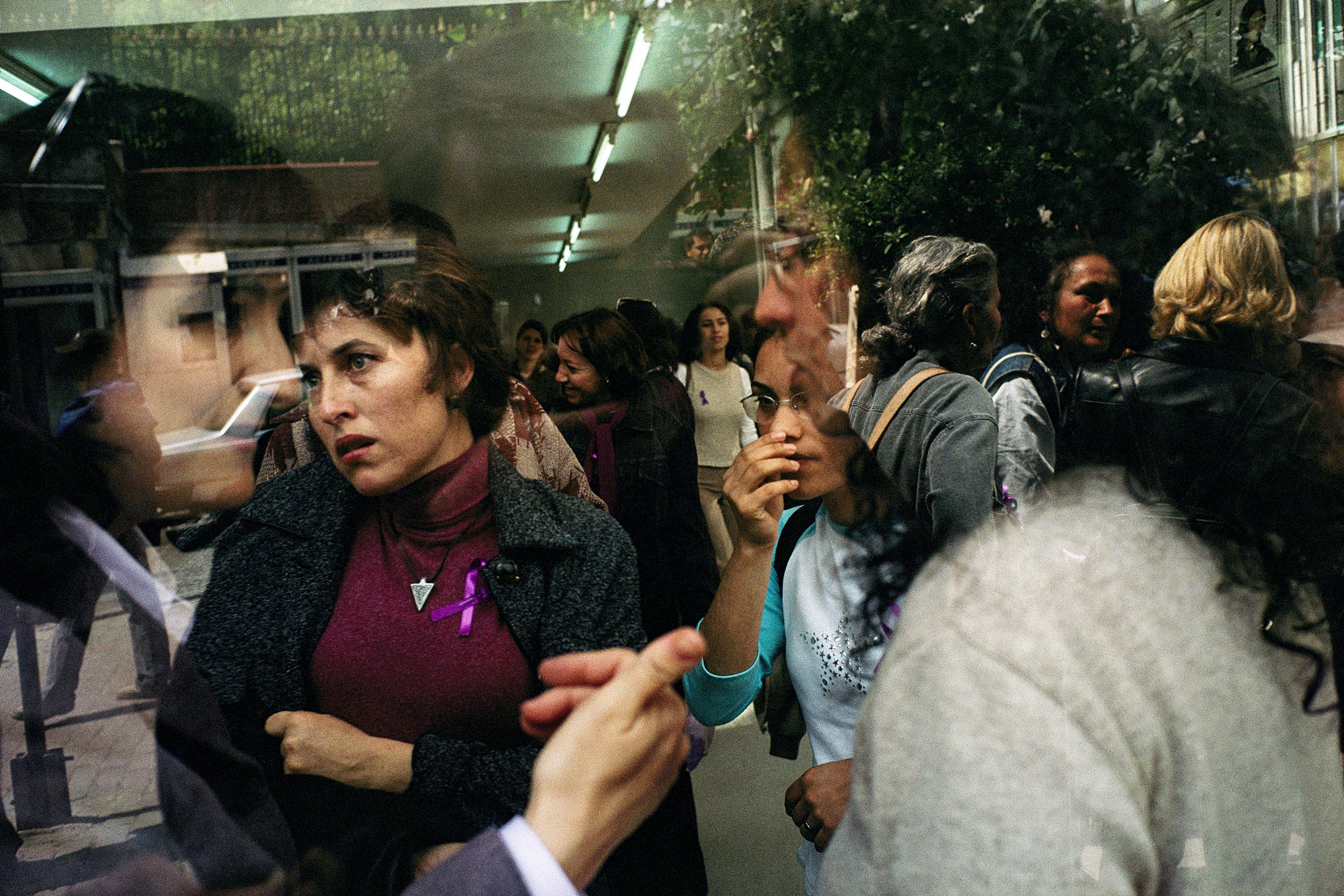 A group of people shown through reflective surfaces creating a layered effect, one wears a purple ribbon.