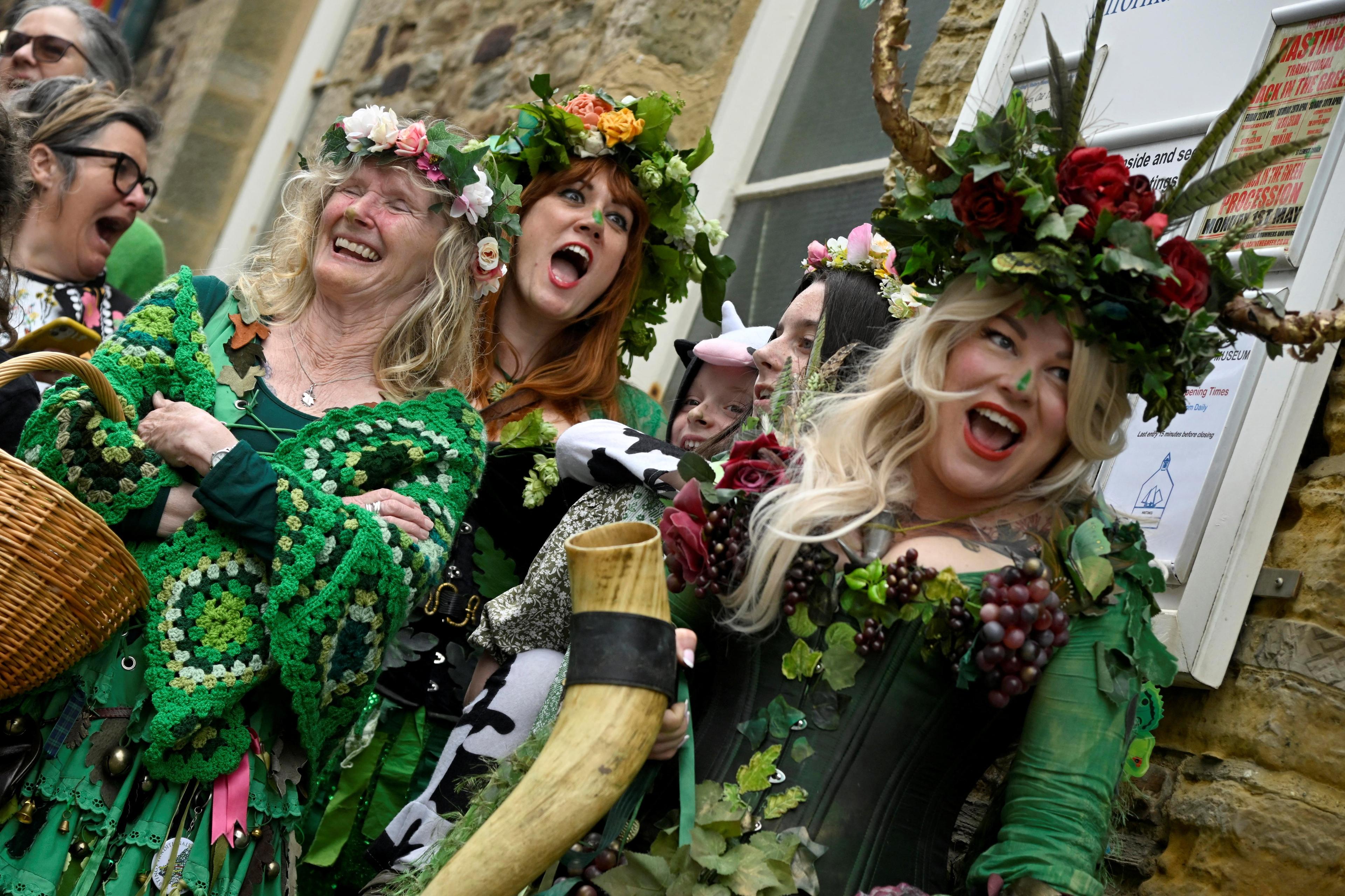 Photo of smiling people in festive nature-inspired costumes with leaves and flowers, outdoors against a stone building.