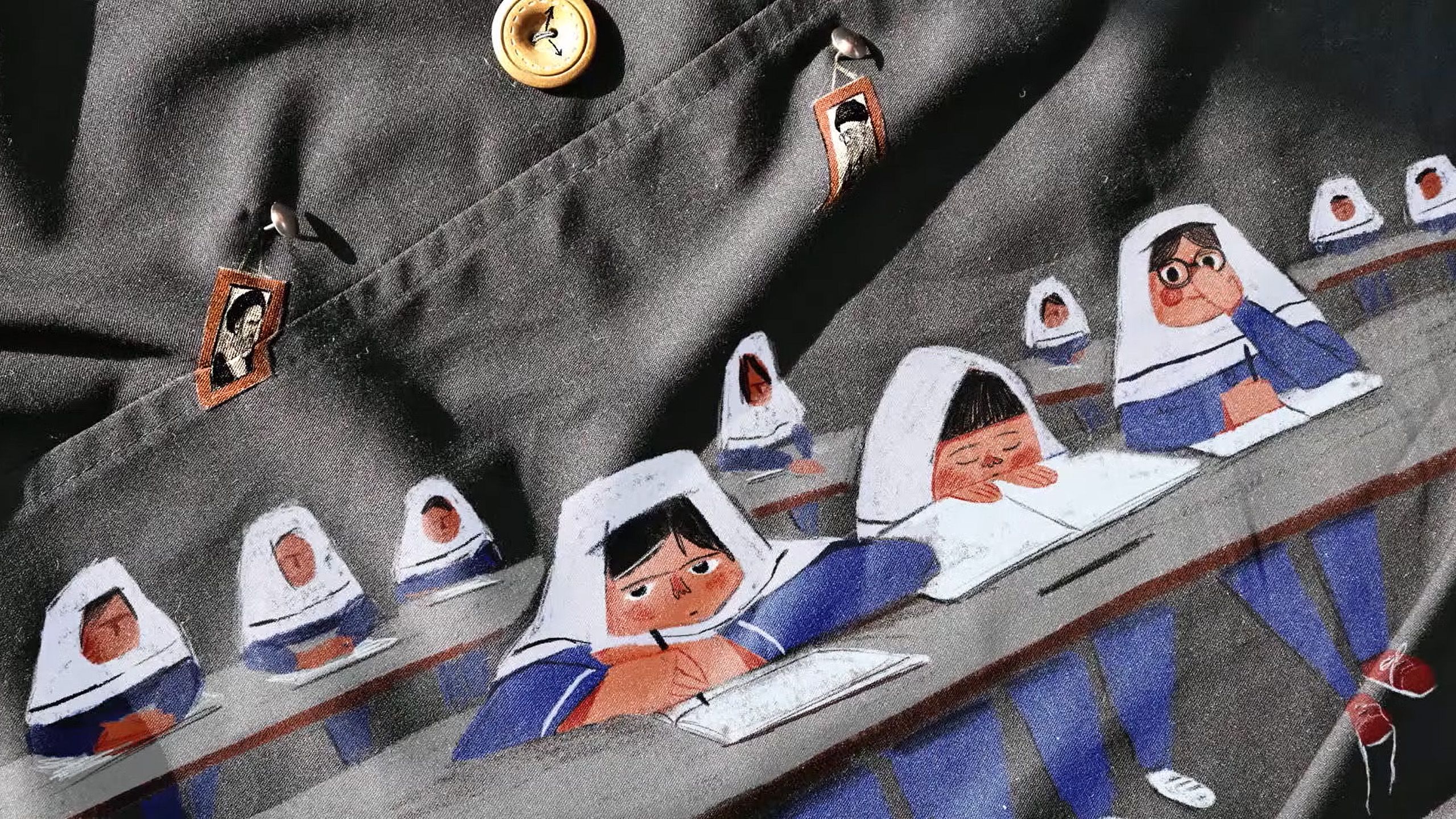 Painting on fabric of students in hijabs writing at desks with a button and small photo on the fabric above.