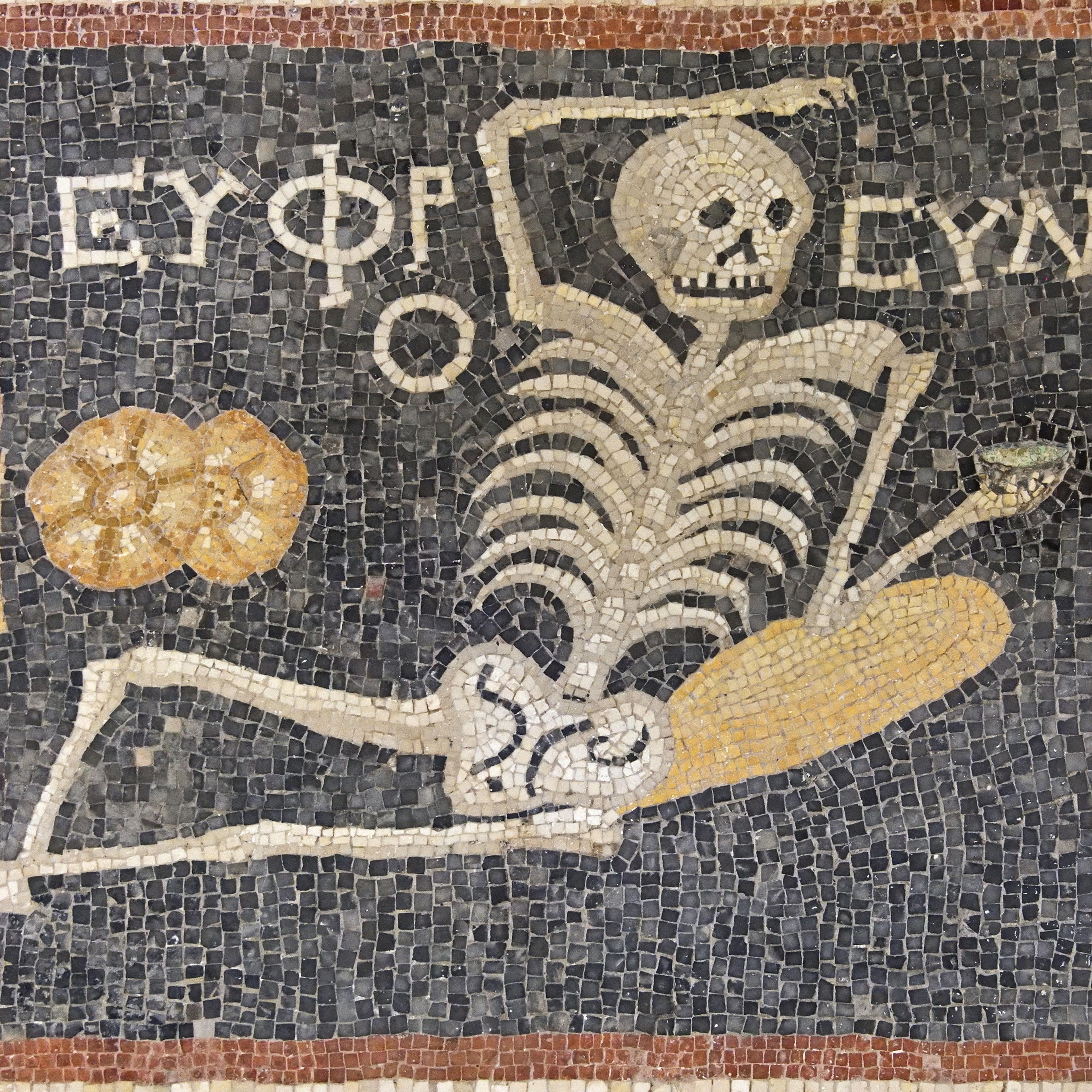 Ancient mosaic depicting a lounging skeleton with Greek text, an amphora, a loaf of bread and a platter on a dark background.