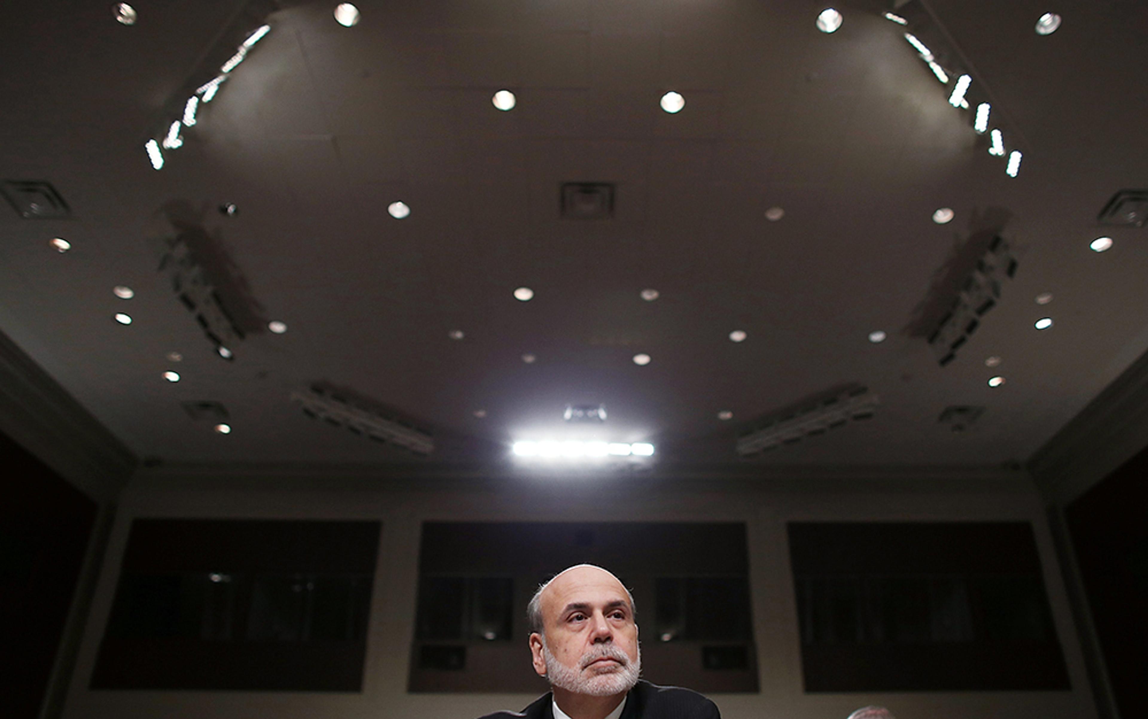 A man with a beard sitting in a large, well-lit room with a high ceiling during an official meeting or conference.