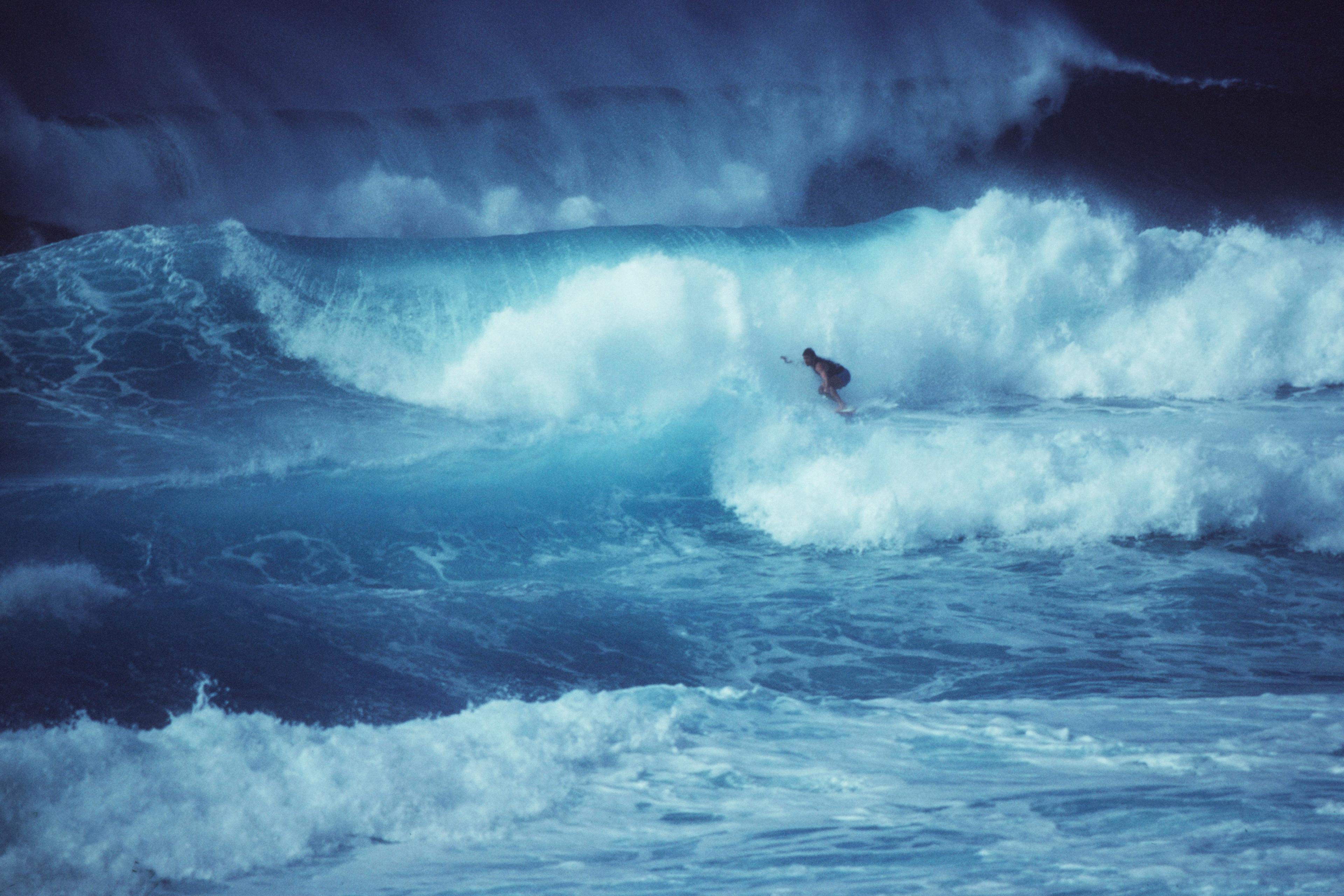 Photo of a surfer riding a large wave in the ocean with cloudy spray, capturing the power and movement of the sea.