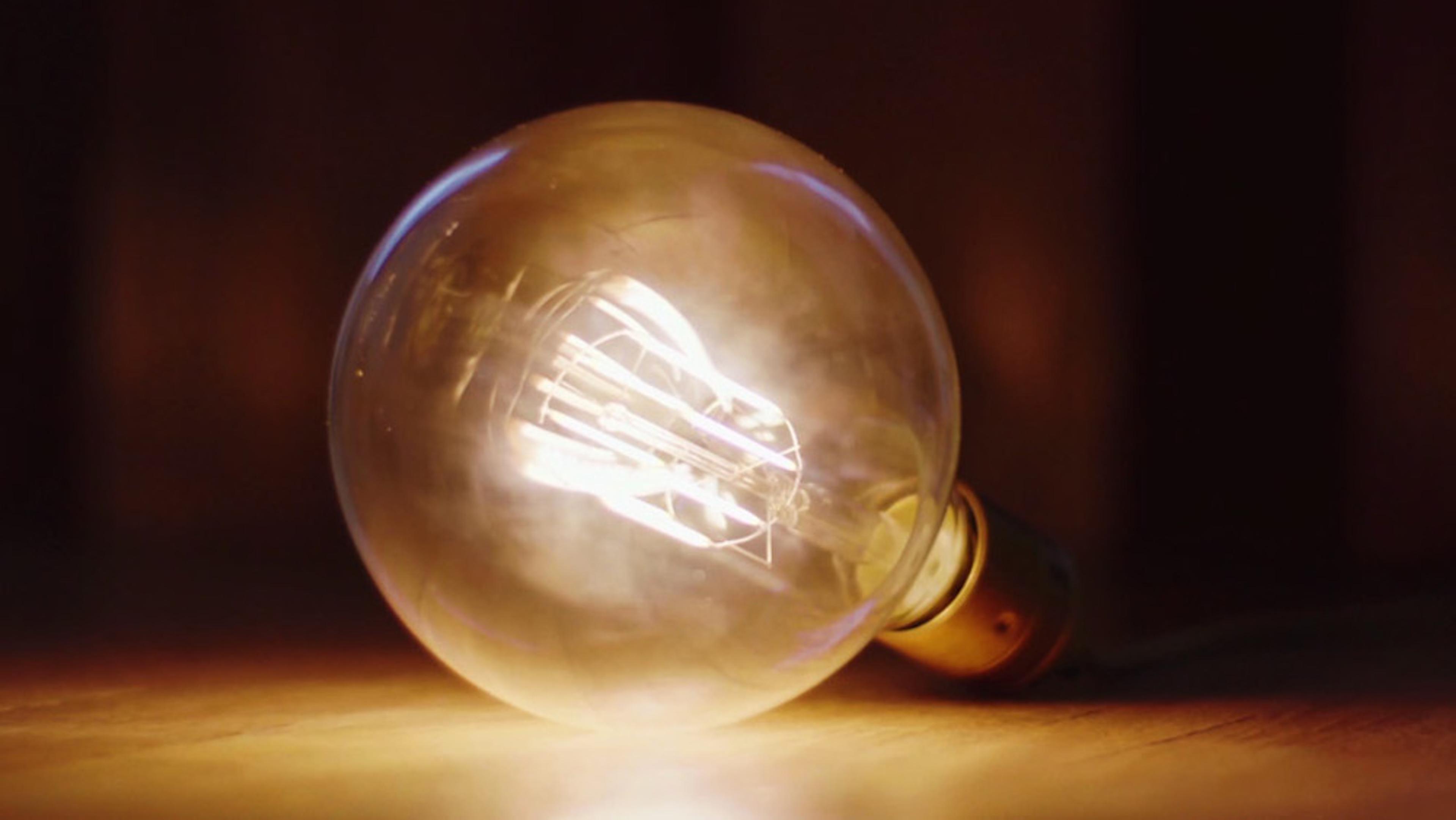 A glowing incandescent light bulb lying on its side on a wooden surface with a dark, blurred background.