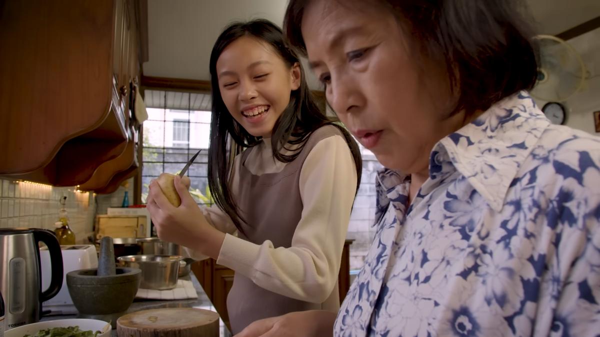 Photo of two women in a kitchen, one peeling a potato while smiling the other focused on cooking, with a mortar in view.