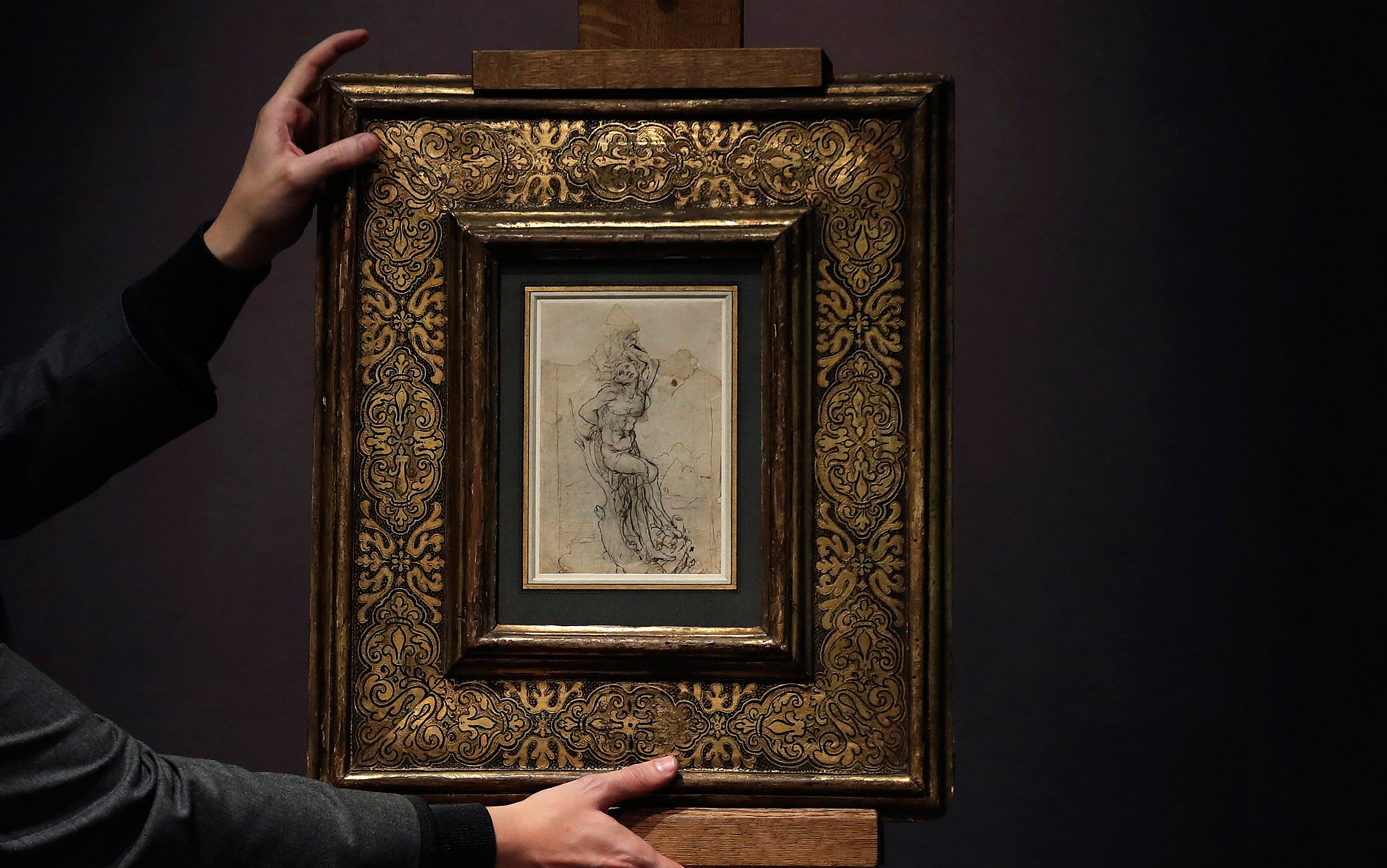 A person holding a framed drawing with ornate golden patterns on the frame against a dark background.