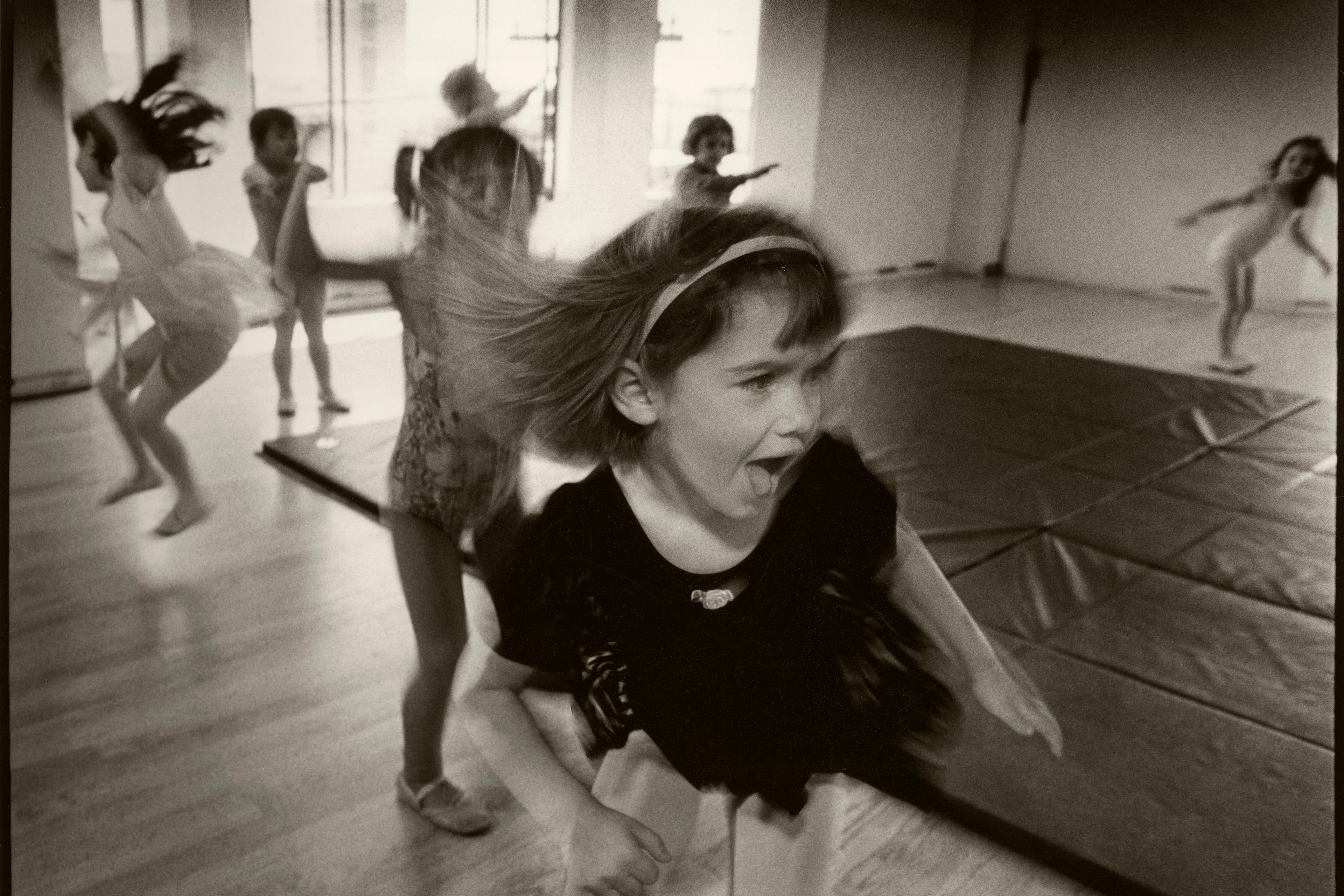 Black and white photo of children dancing energetically in a studio, with a girl in the foreground expressing excitement.