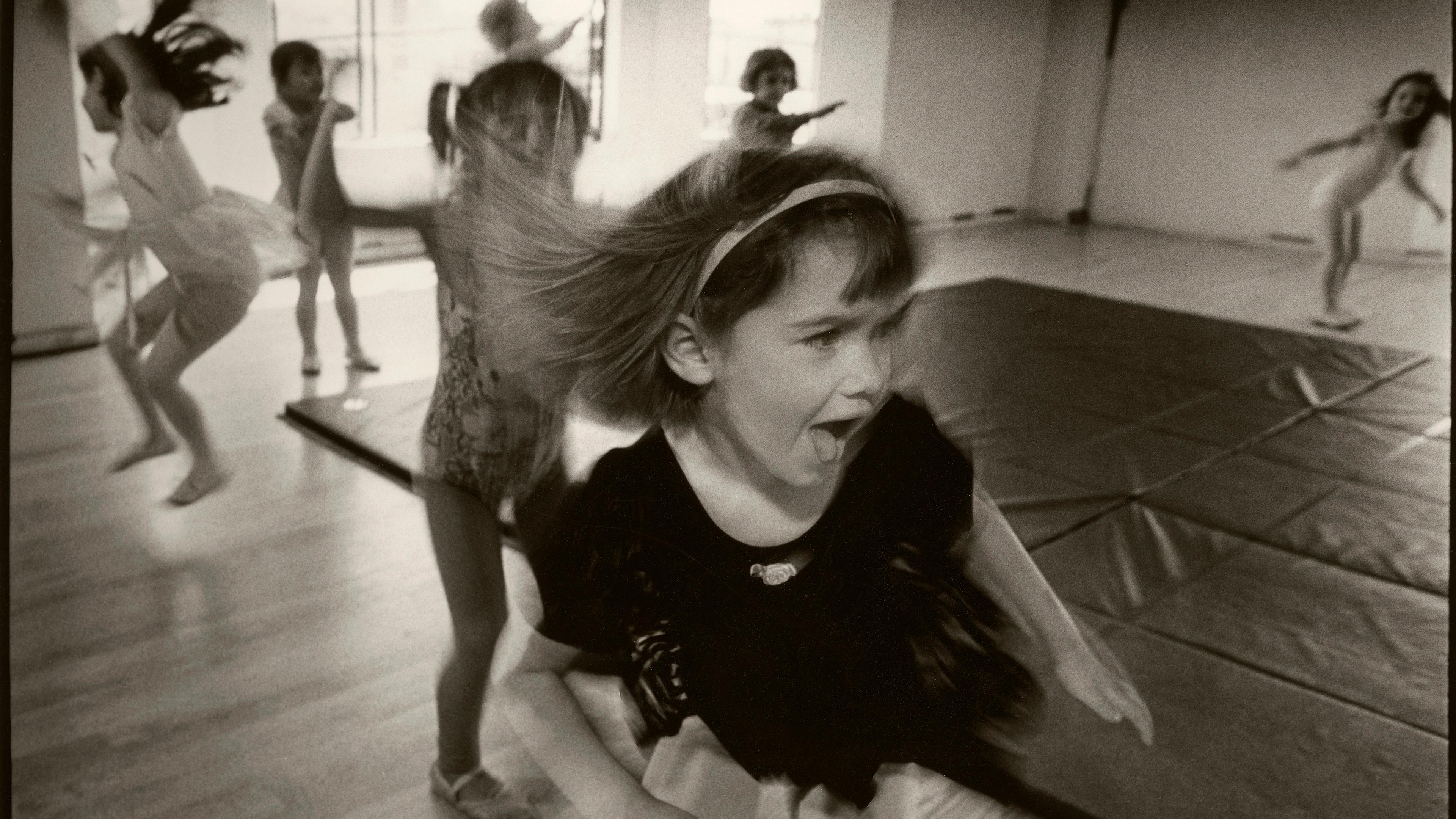 Black and white photo of children dancing energetically in a studio, with a girl in the foreground expressing excitement.